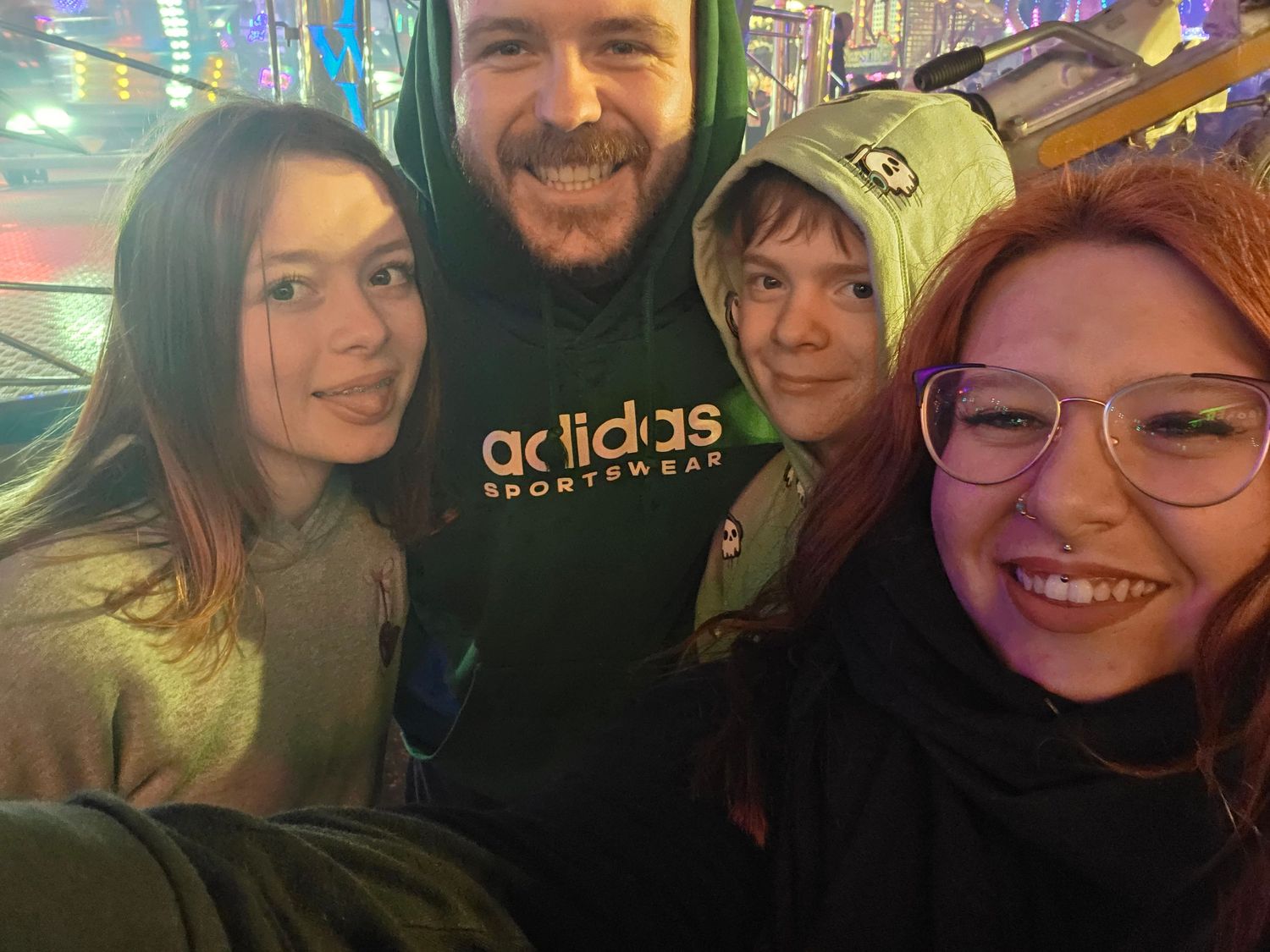 Group of four friends taking a selfie at a colorful fairground at night.
