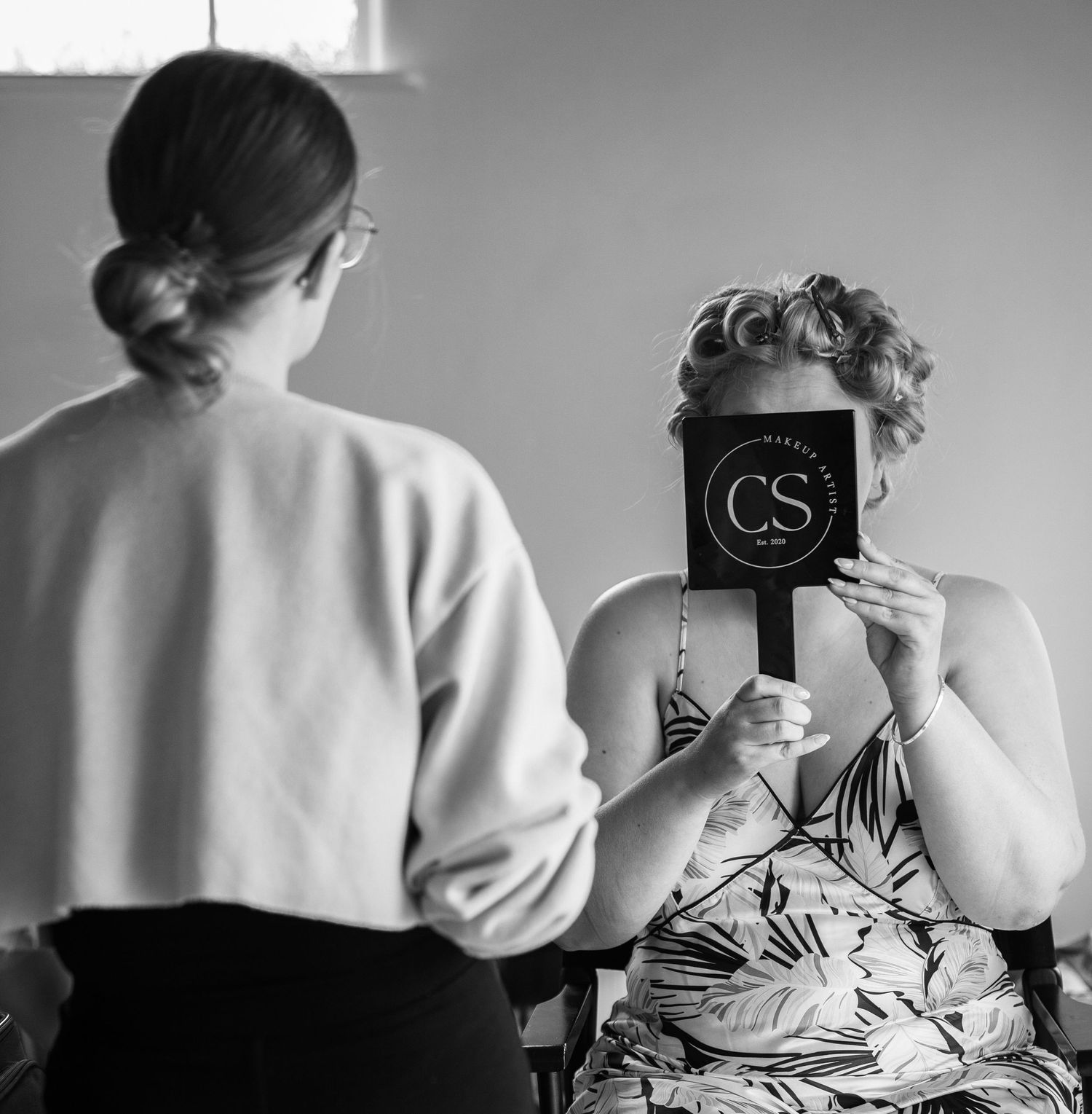 Black and white photo of a woman holding a CS makeup mirror during bridal preparations.