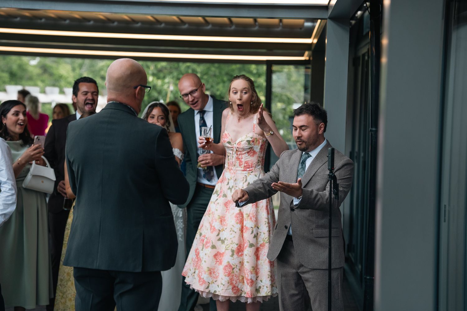Wedding guests mingling and chatting outdoors near a modern glass venue building.