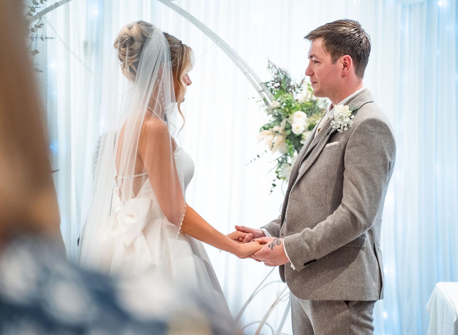 Bride and groom exchange vows at wedding altar adorned with white flowers and greenery.