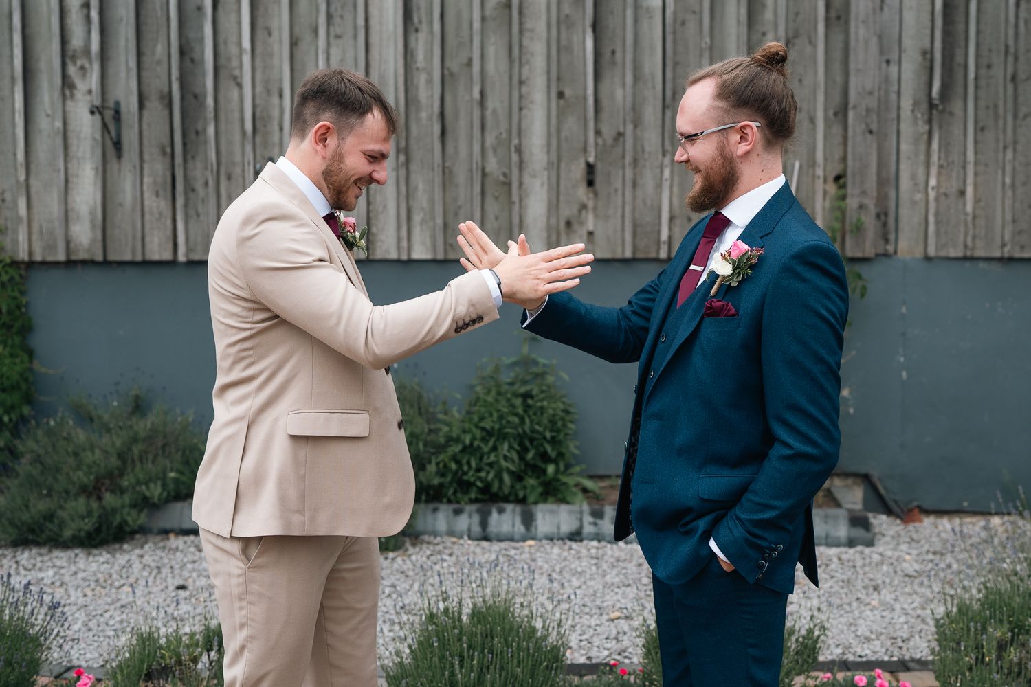 Two groomsmen in suits sharing a joyful high-five moment outdoors at The barn at willerby Hill in Hull East Yorkshire