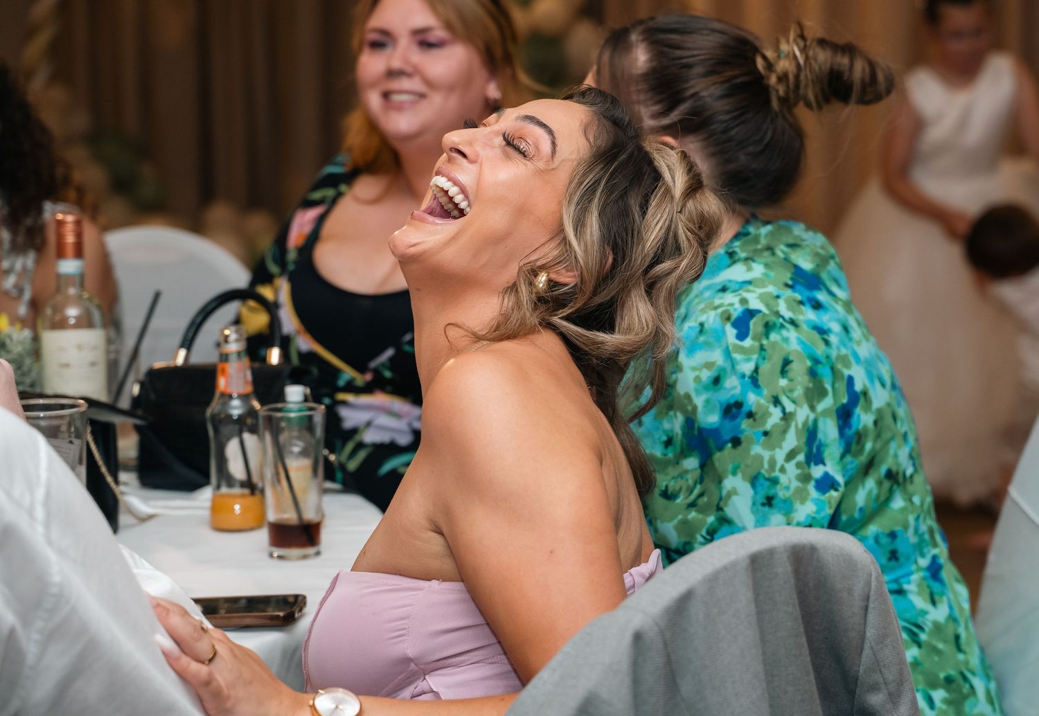 Wedding guest laughs joyfully while seated at decorated table during wedding reception.