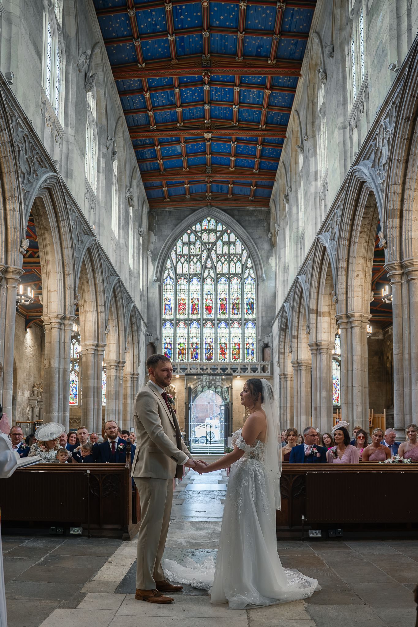 Bride and groom holding hands at the altar of a grand cathedral with ornate blue ceiling.