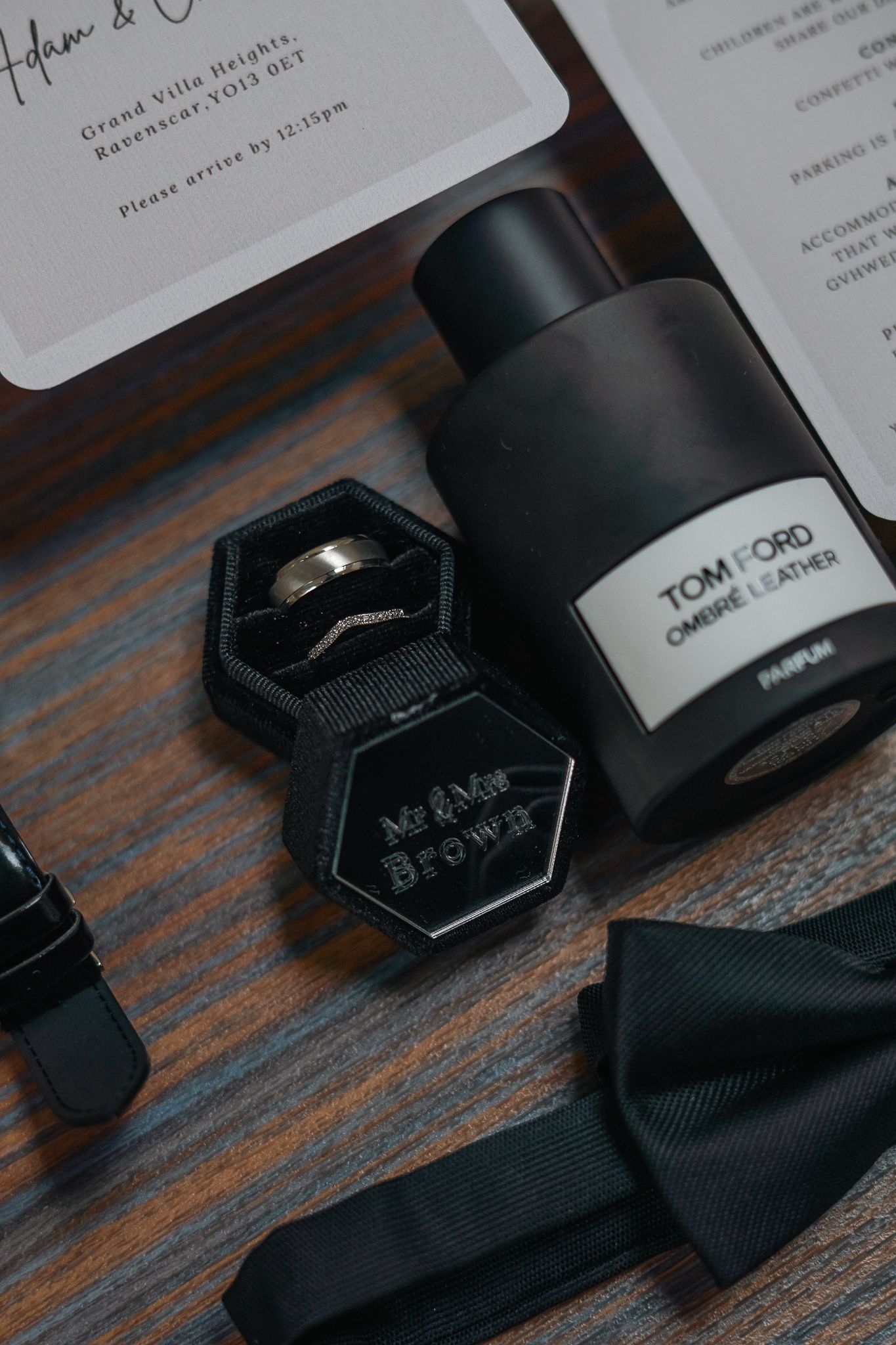 Wedding flat lay featuring Tom Ford Ombre Leather parfum, ring box with bands, black bow tie, and invitation at Grand villa heights