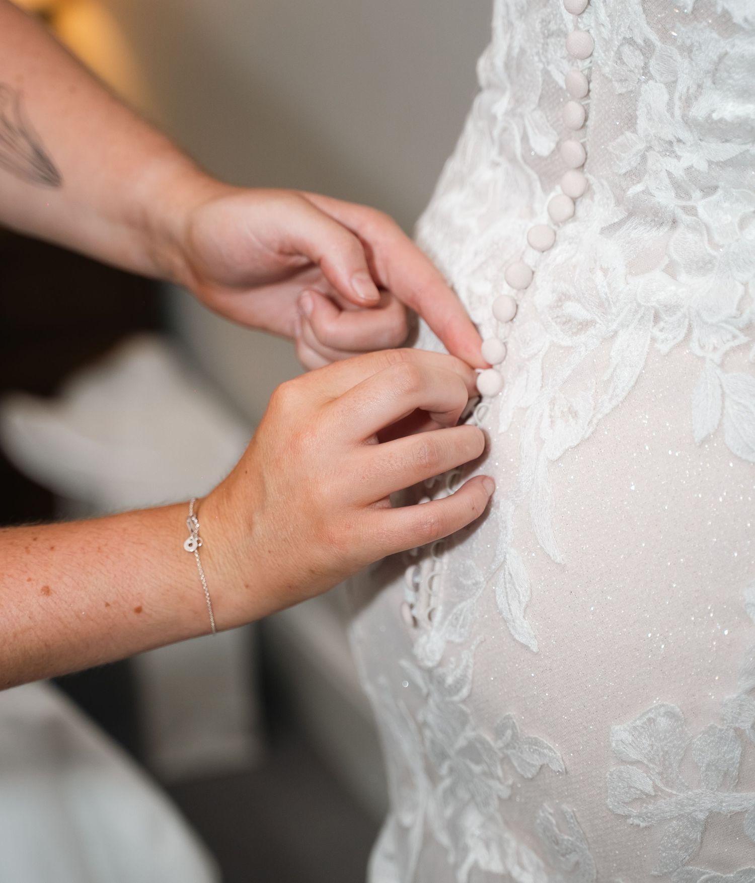 Close-up of hands buttoning intricate lace buttons on back of bridal wedding gown.