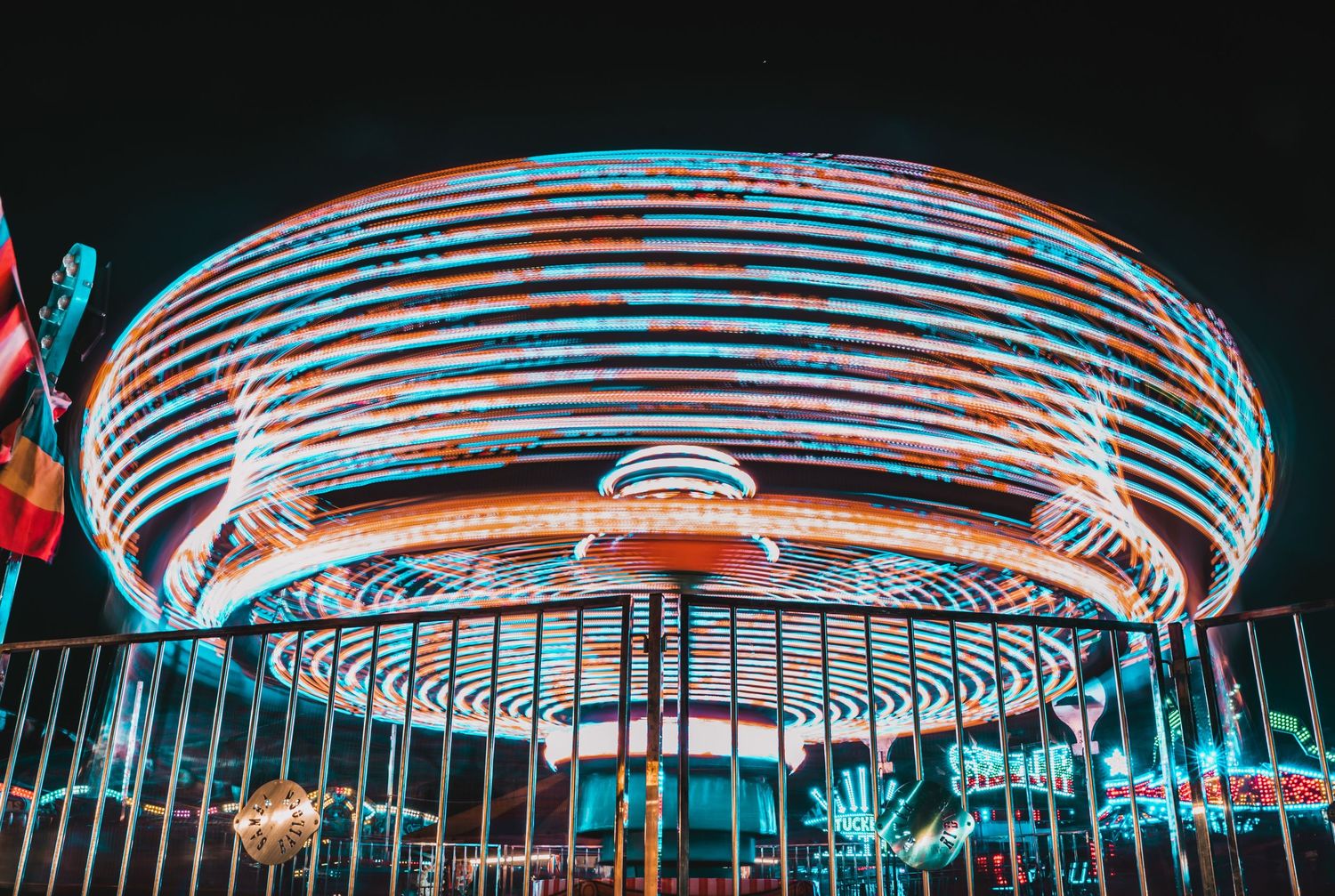 Long exposure photo of a spinning fairground ride with colorful light trails at night.