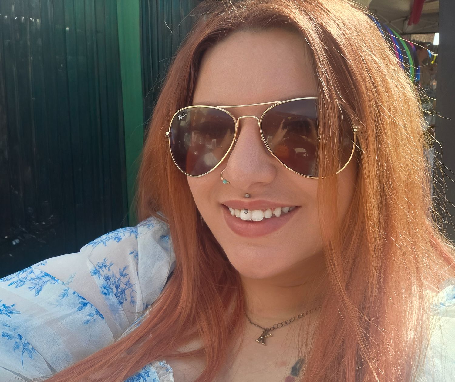 Smiling redhead woman with nose ring wearing aviator sunglasses in sunny outdoor selfie.