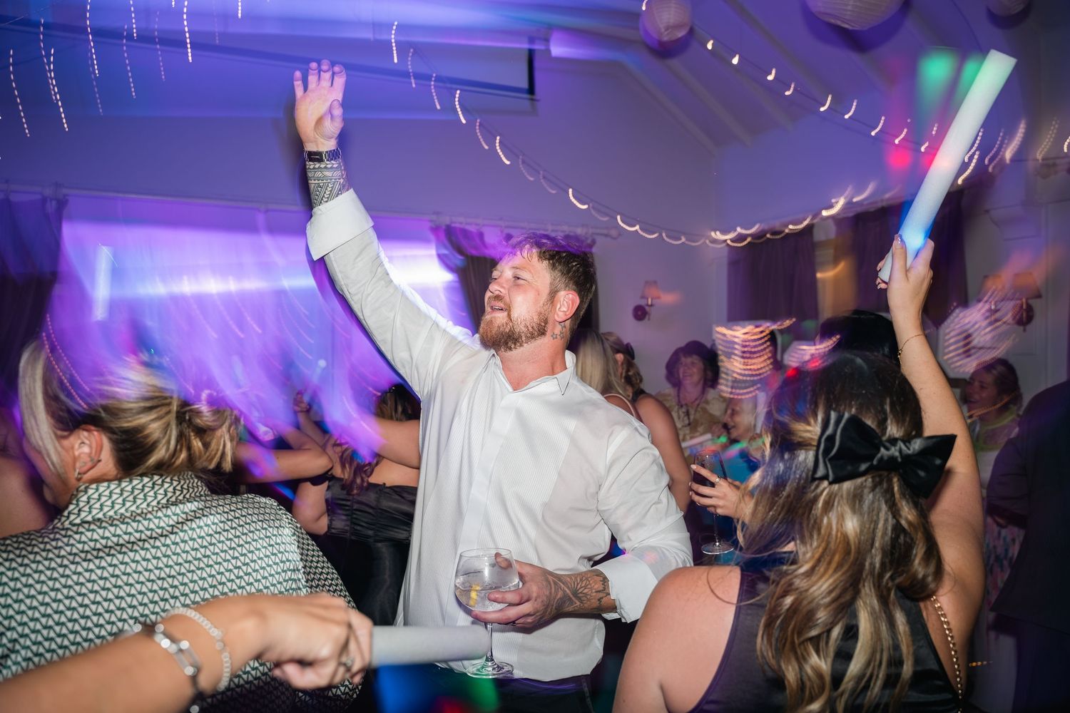 Excited wedding guest raises arm while dancing at lively evening wedding reception party.