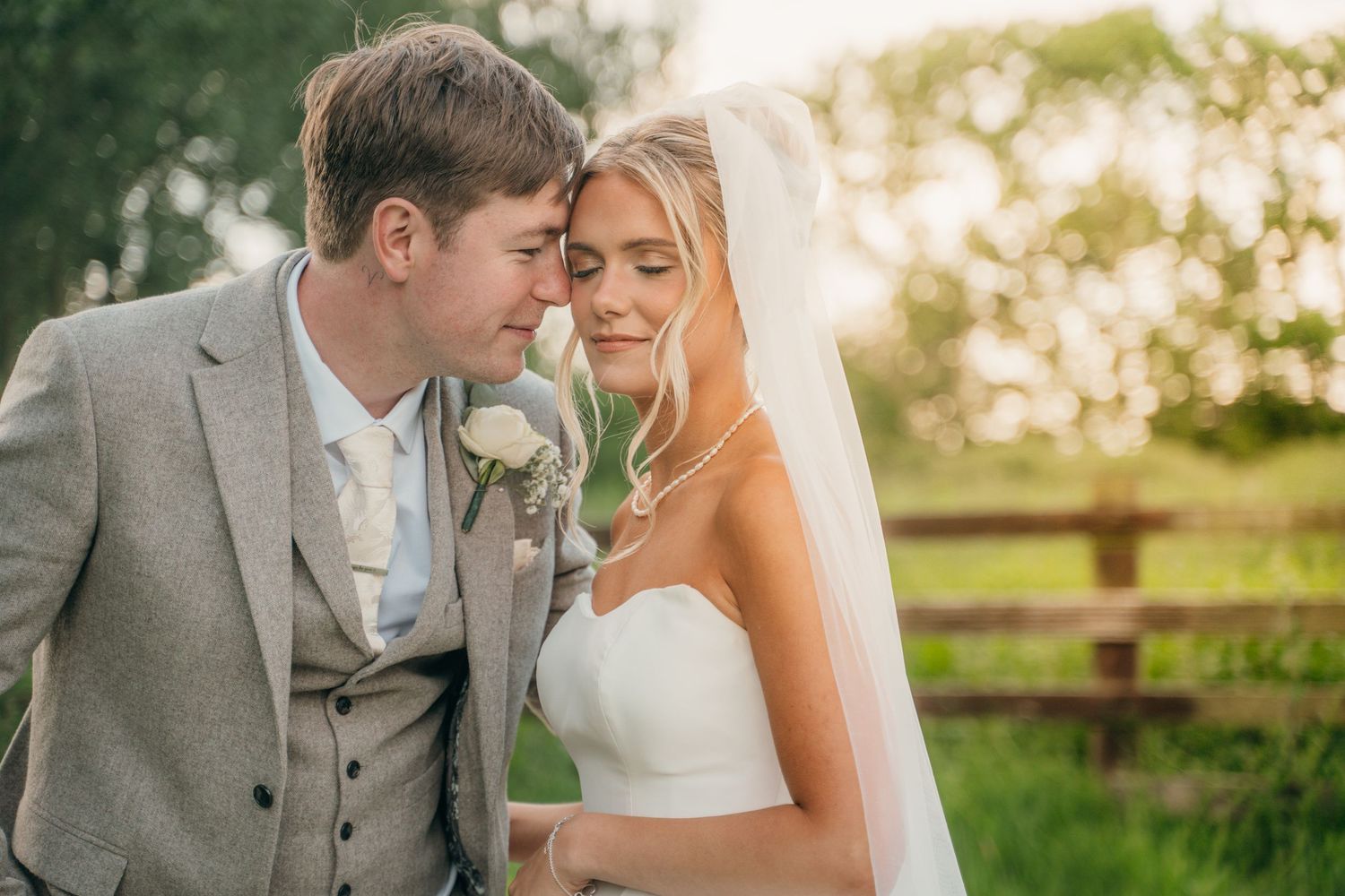 Bride and groom sharing a tender moment in golden hour light by a wooden fence.