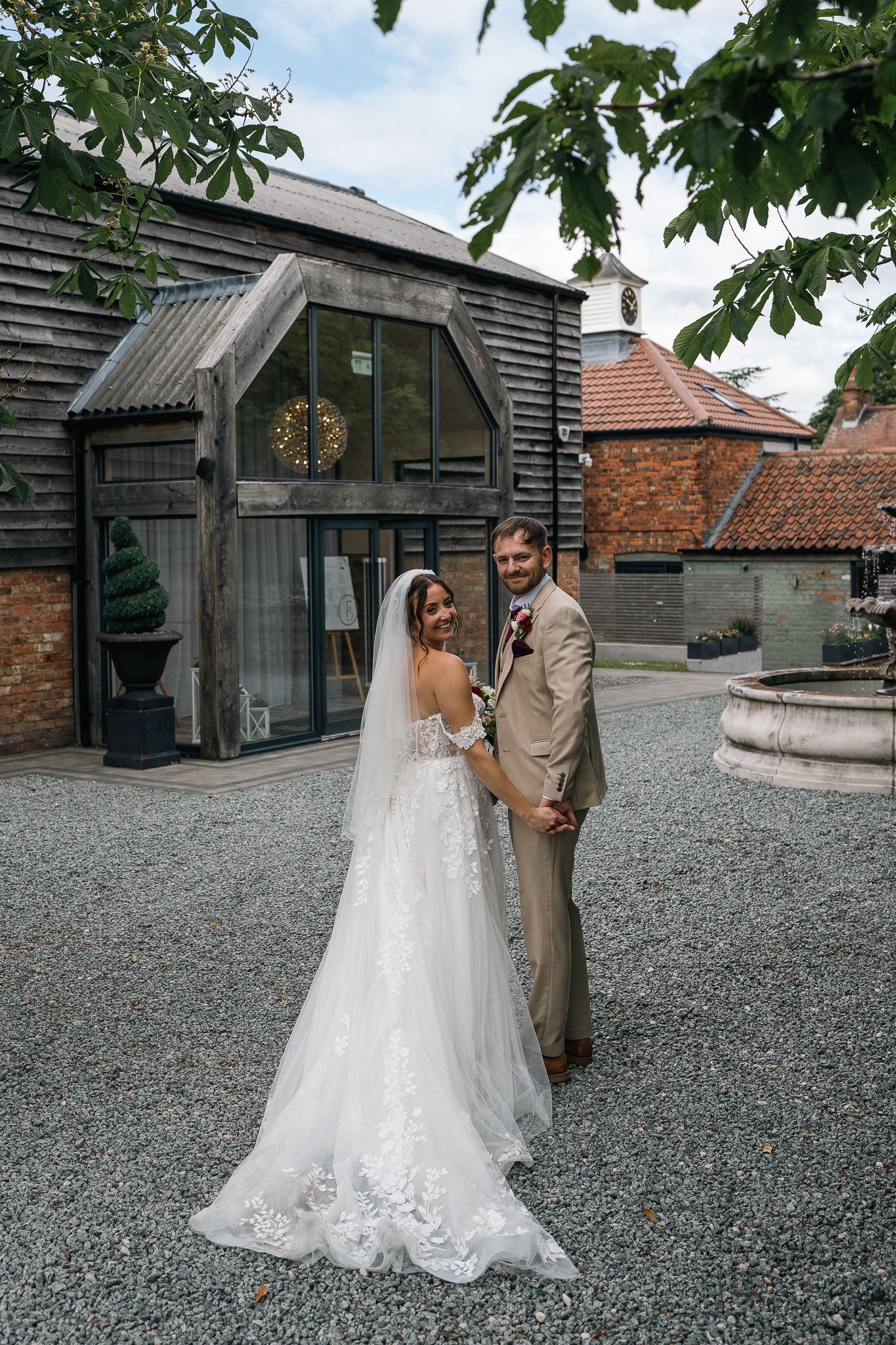 Bride and groom posing together outside a rustic barn wedding venue on a cloudy day.