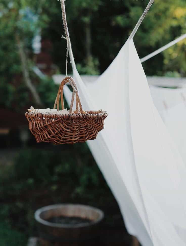 Laundered sheets hanging on a line. Woven cane little basket hanging that holds the pegs. Laundry help in Canberra. Home laundry Bowral.
