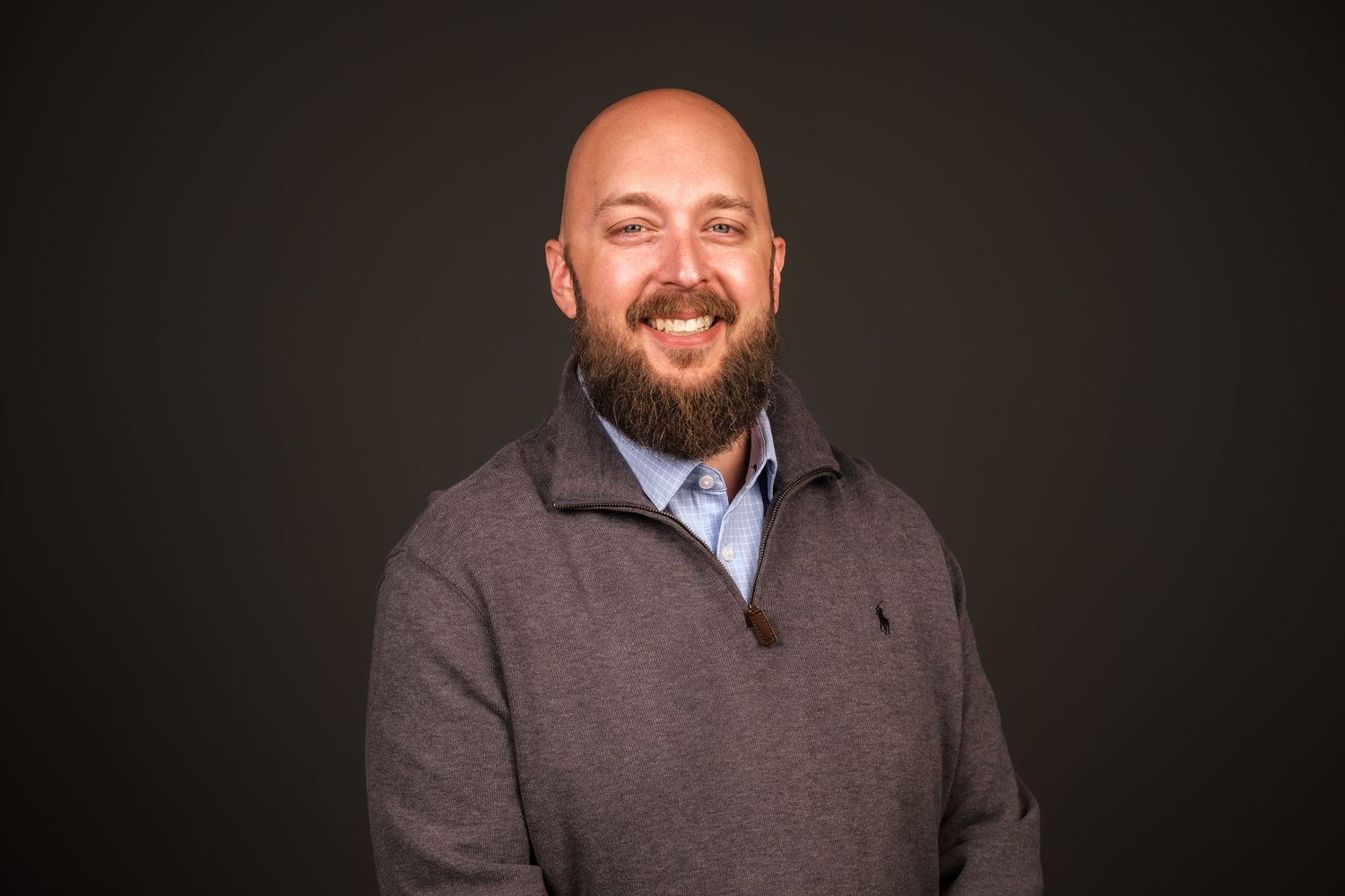 Professional headshot of a smiling bearded man in gray pullover against a dark studio background, photographed by Echo Studio in Huntsville.
