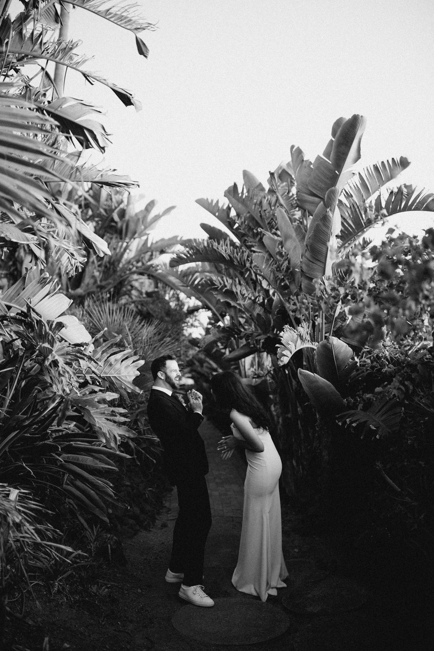 Bride and groom standing together beneath tropical plants in their backyard
