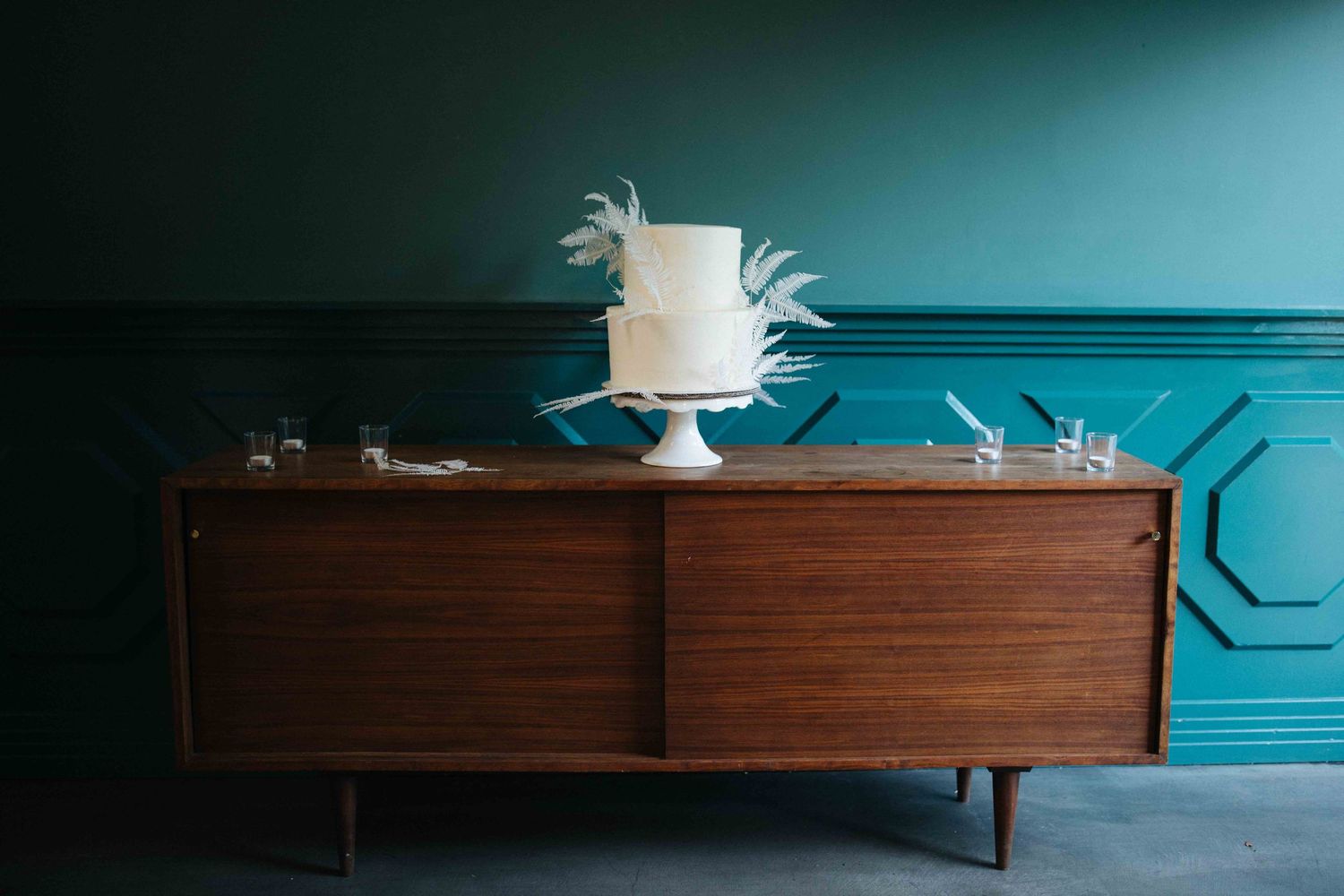 A mid-century modern sideboard with tapered legs sits against a turquoise wall with decorative molding.