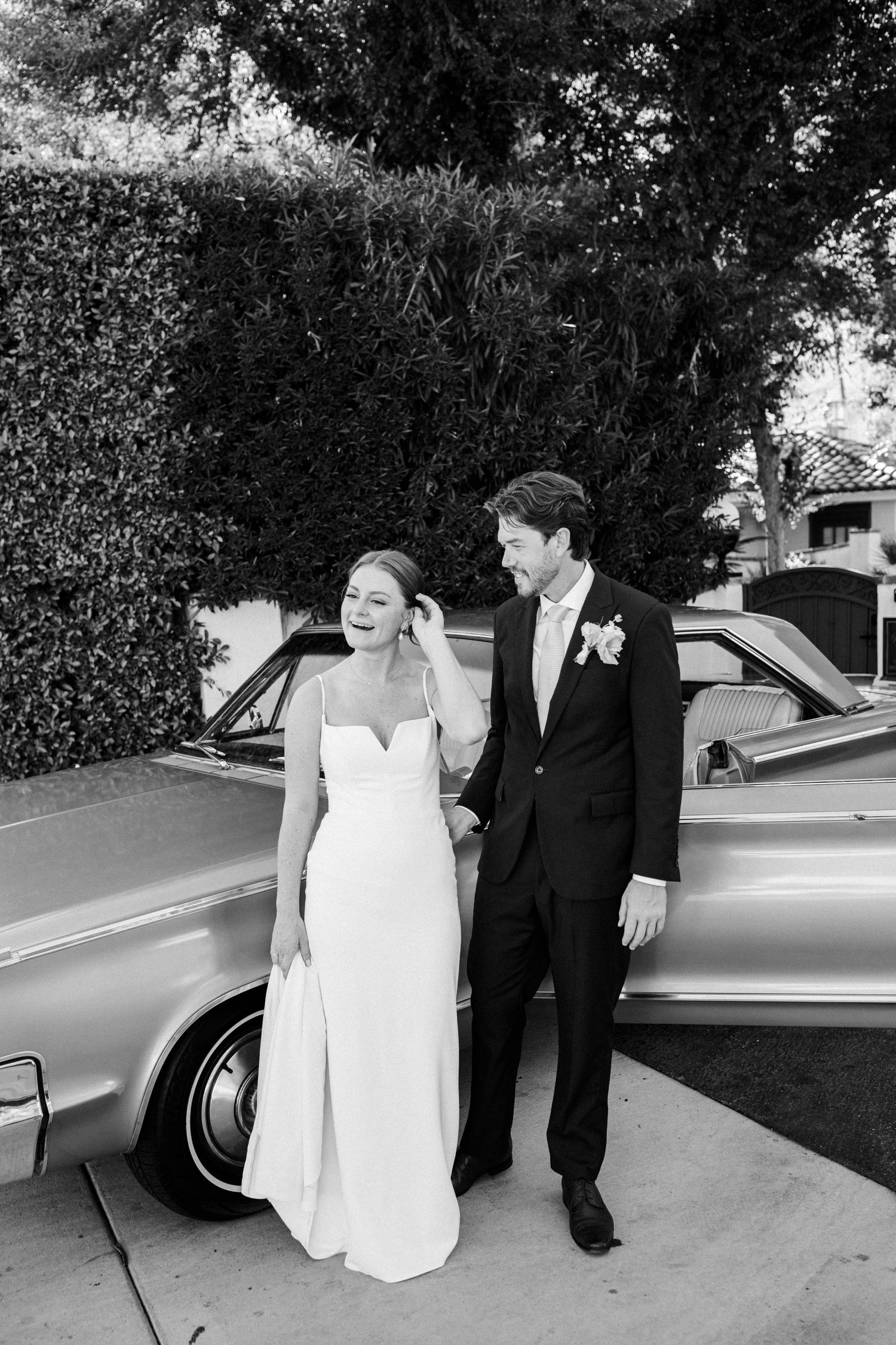 Bride and groom standing beside a vintage car in a candid wedding moment