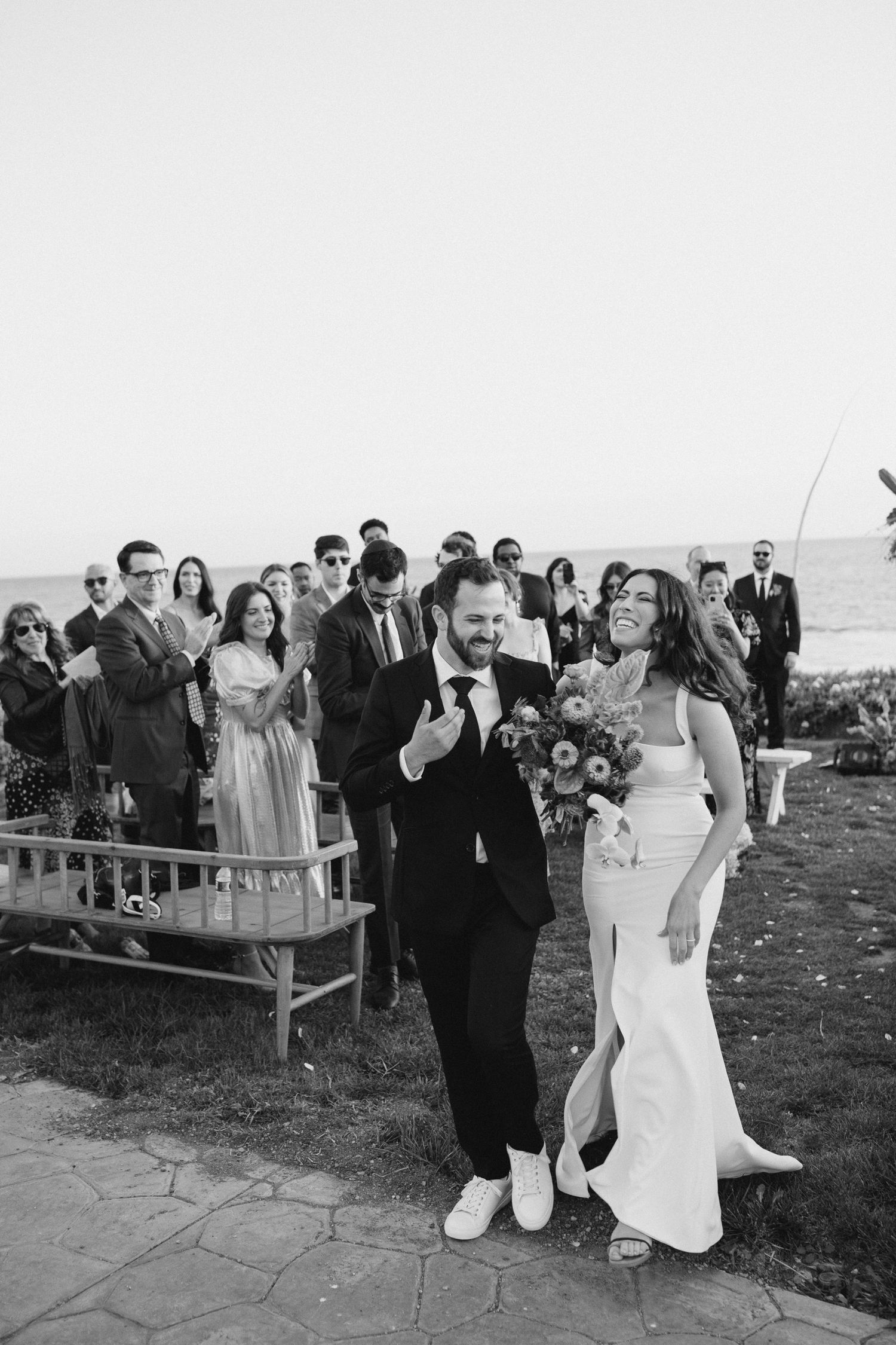 Wedding guests celebrate during an outdoor reception on a stone patio overlooking a scenic view.