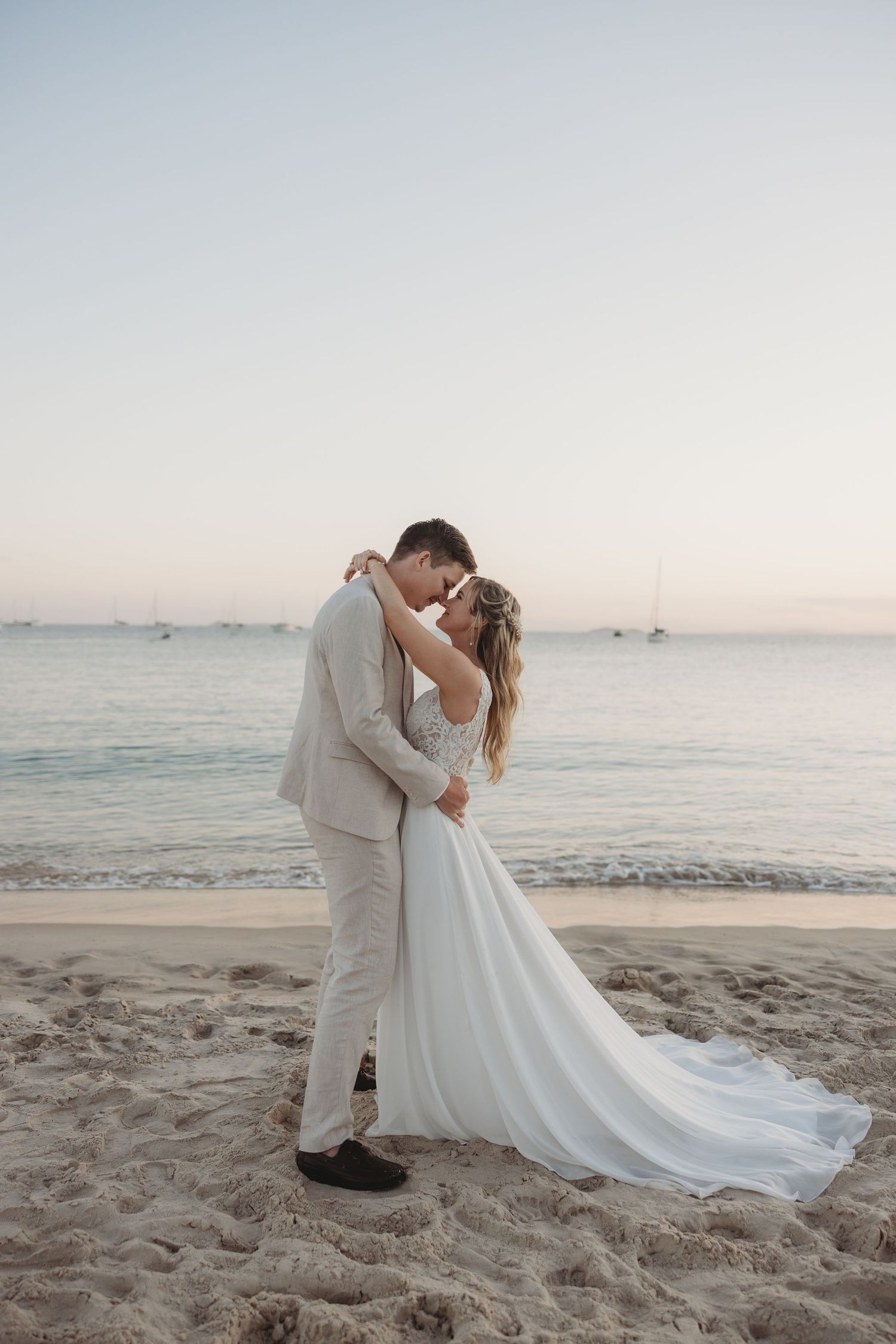 A romantic beach photoshoot captures an intimate moment between a couple at sunset.