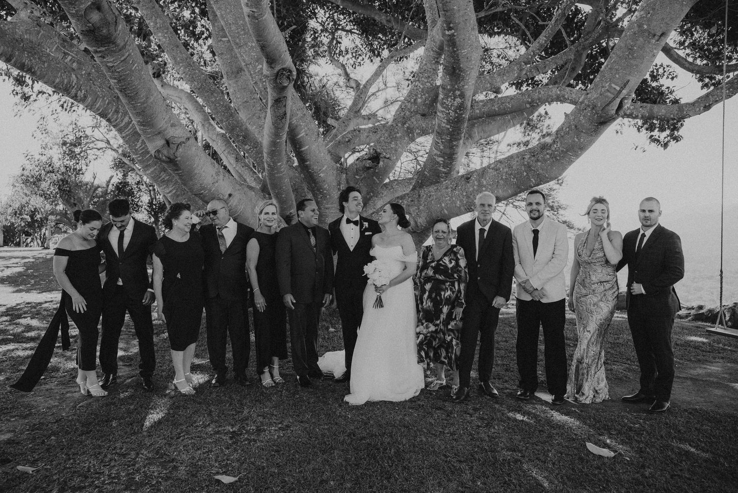 Wedding party poses under a large tree for formal group photos.