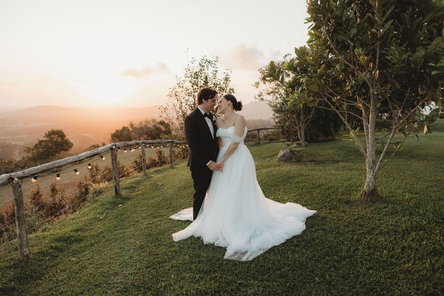 Wedding couple shares tender moment on landscaped hilltop during golden hour.