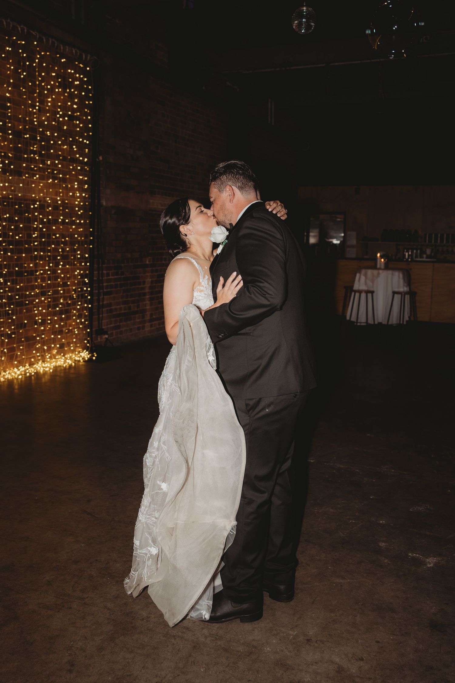 A romantic first dance moment between newlyweds in front of a twinkling light wall at their reception.