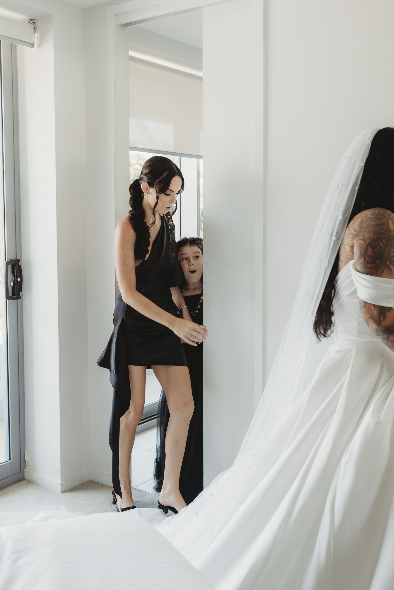 Wedding preparations in a bright room with a black dress and flowing white veil visible.