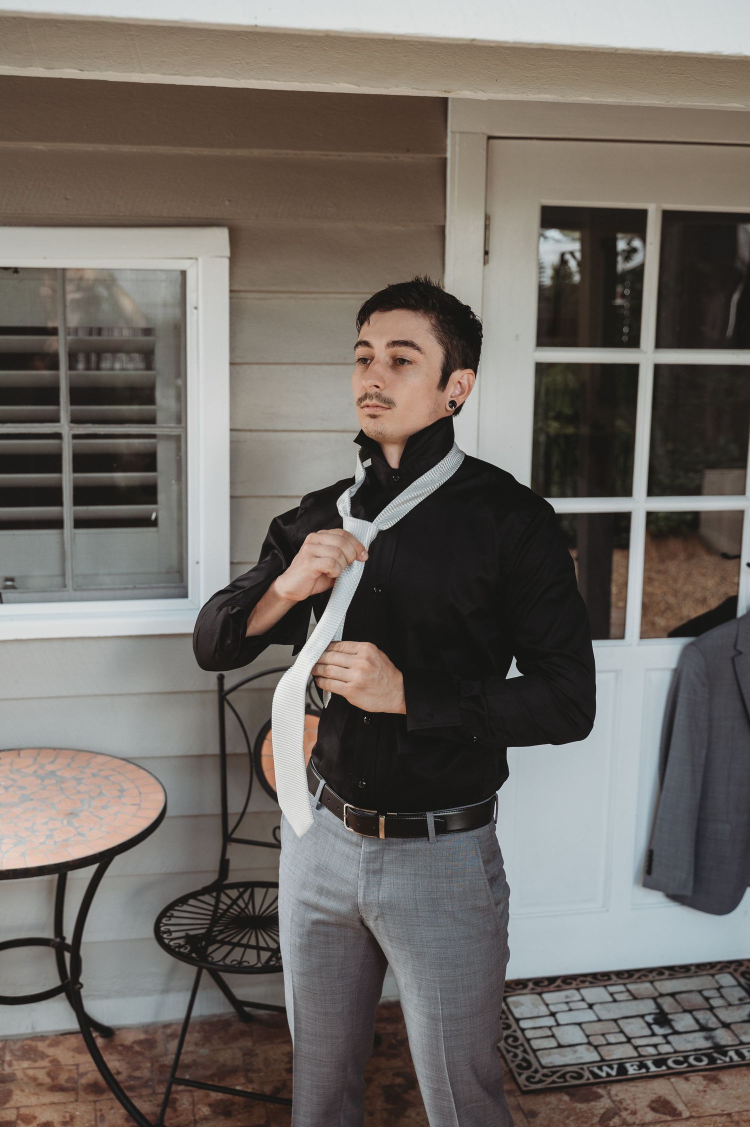 Person adjusting formal attire while getting ready on an outdoor porch. Groom prep Rockhampton Wedding