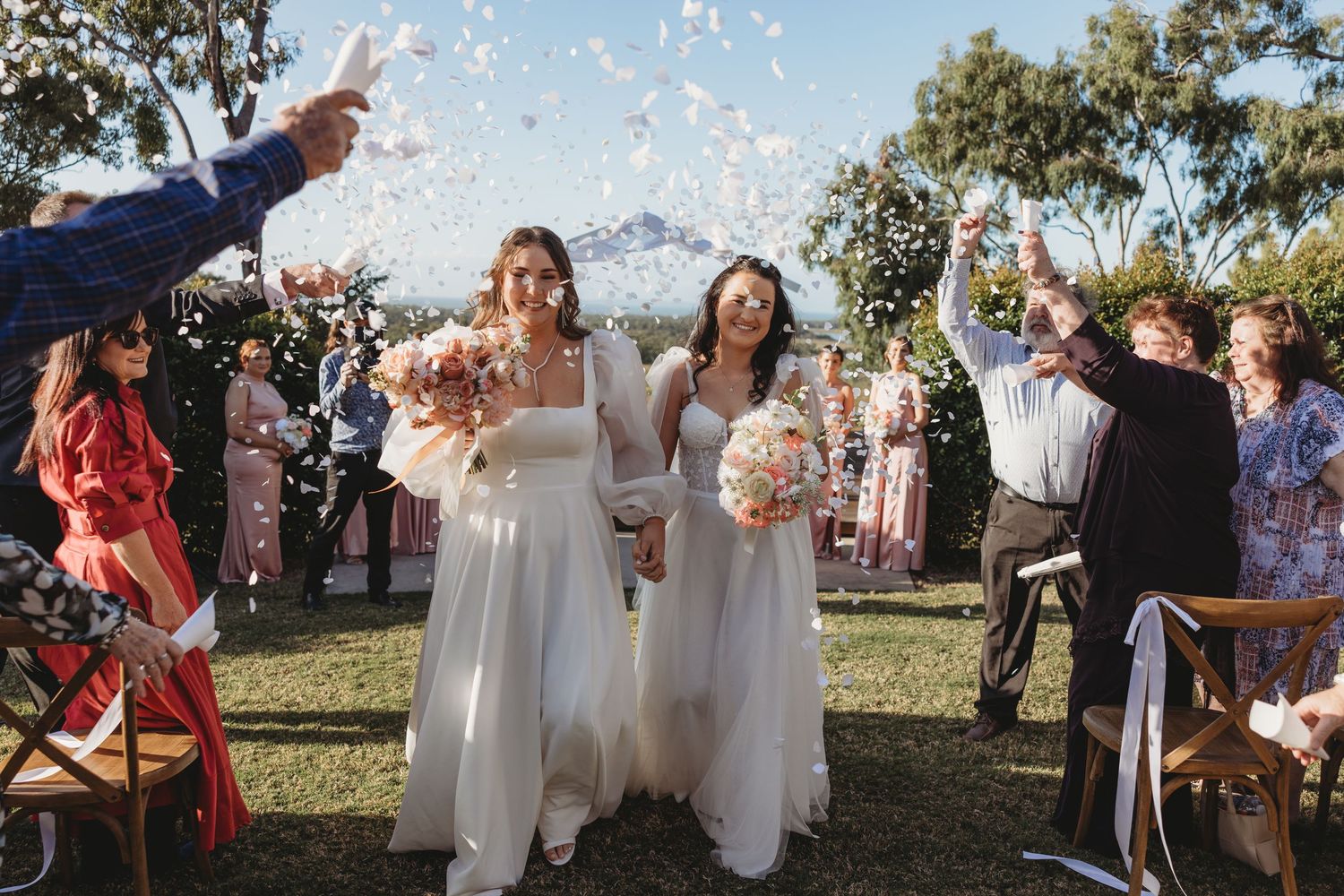 Wedding guests celebrate with confetti toss during outdoor daytime ceremony.