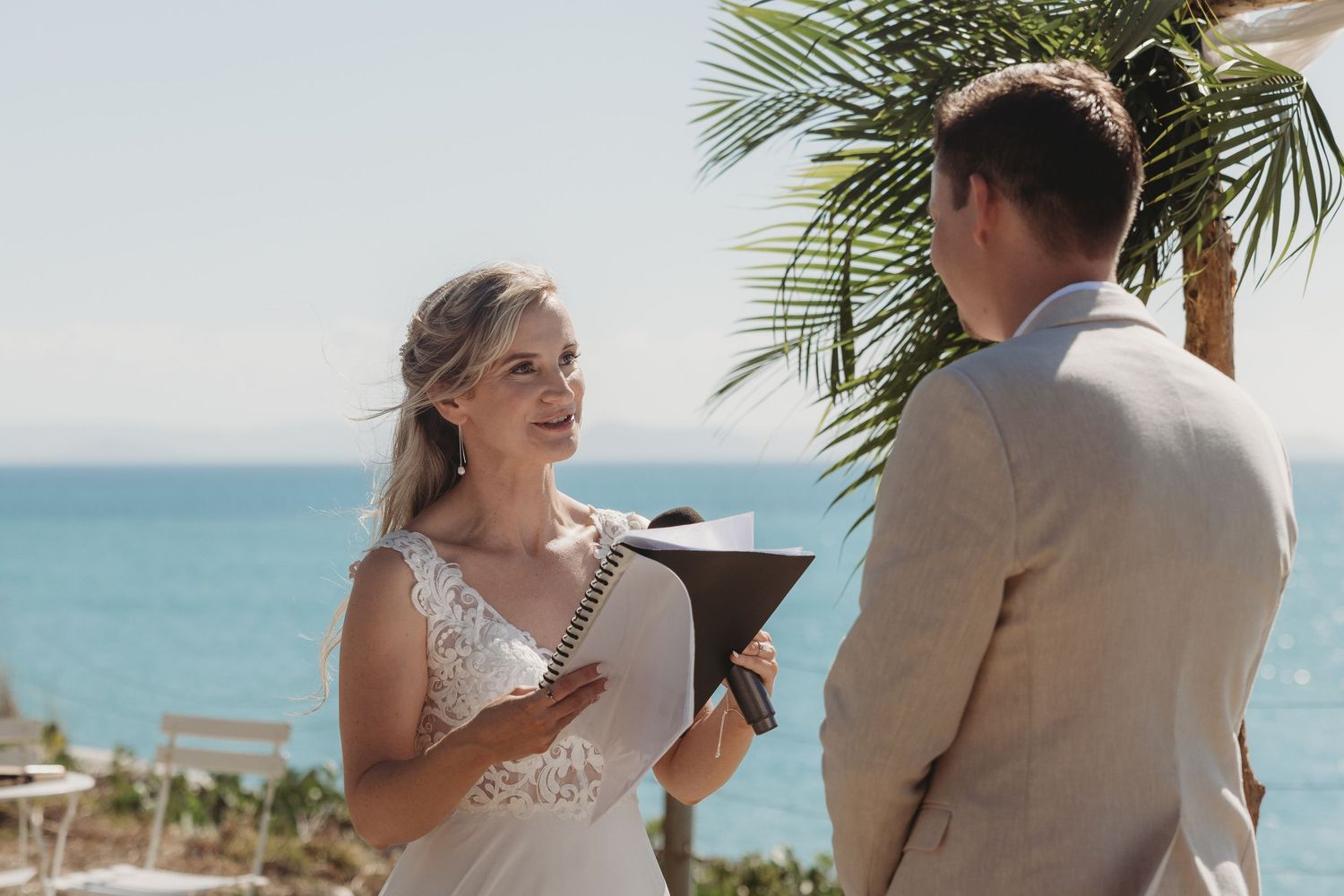 Beachside wedding ceremony with couple sharing joyful moments under bright blue sky.