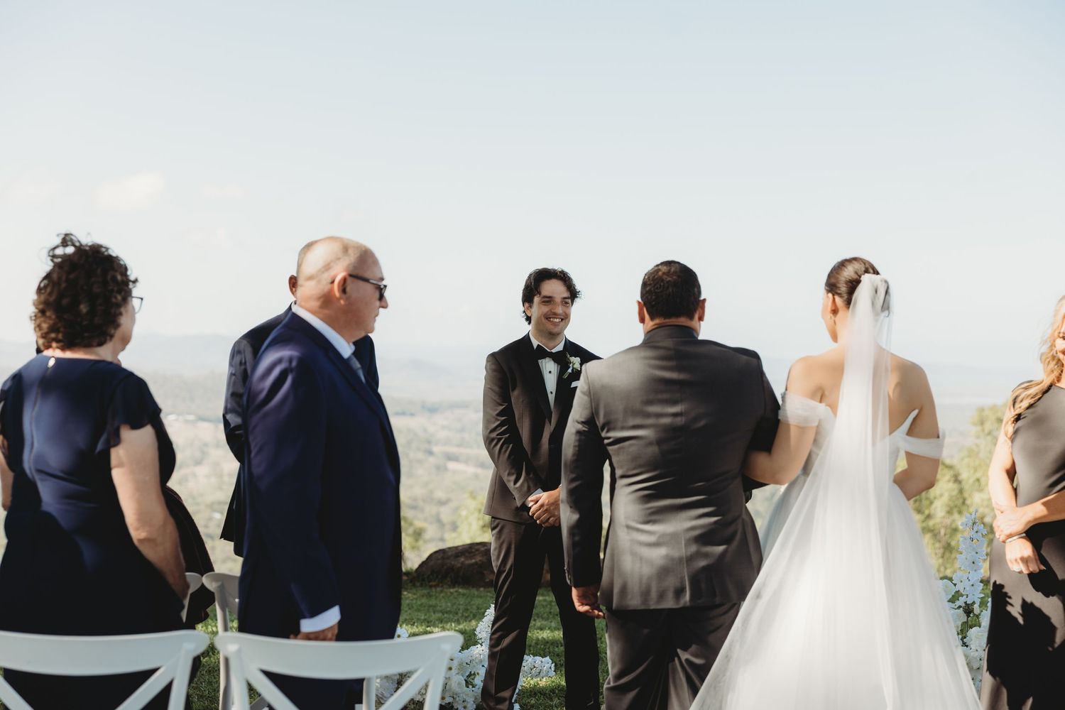 Outdoor wedding ceremony setup on a hilltop with white chairs and scenic mountain views in the background.