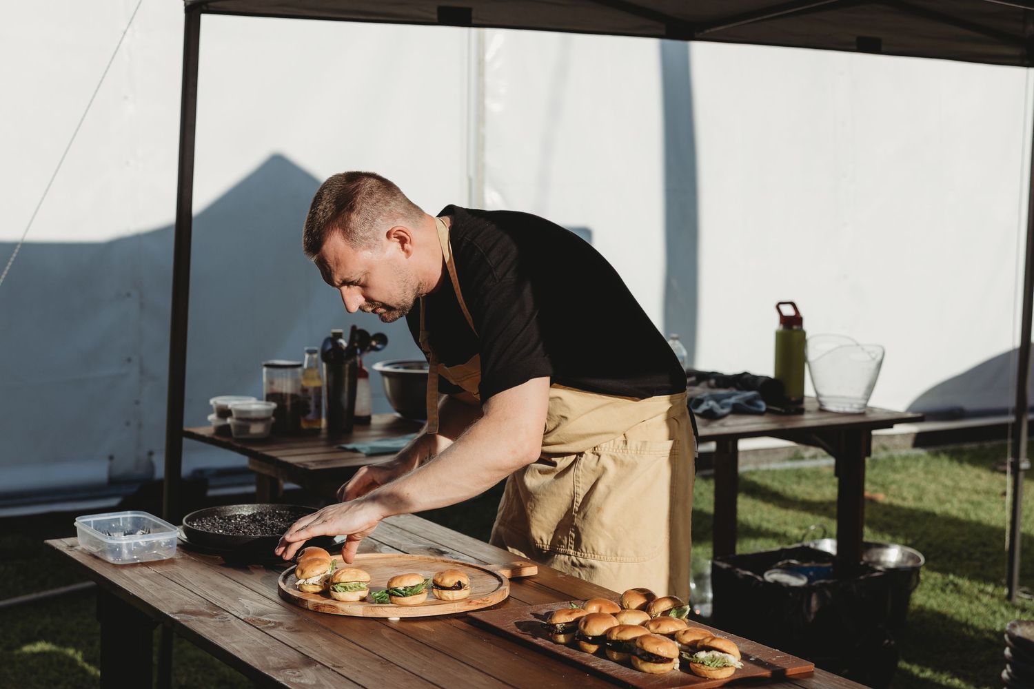 Food service workers plating dishes on long wooden tables at an outdoor venue.