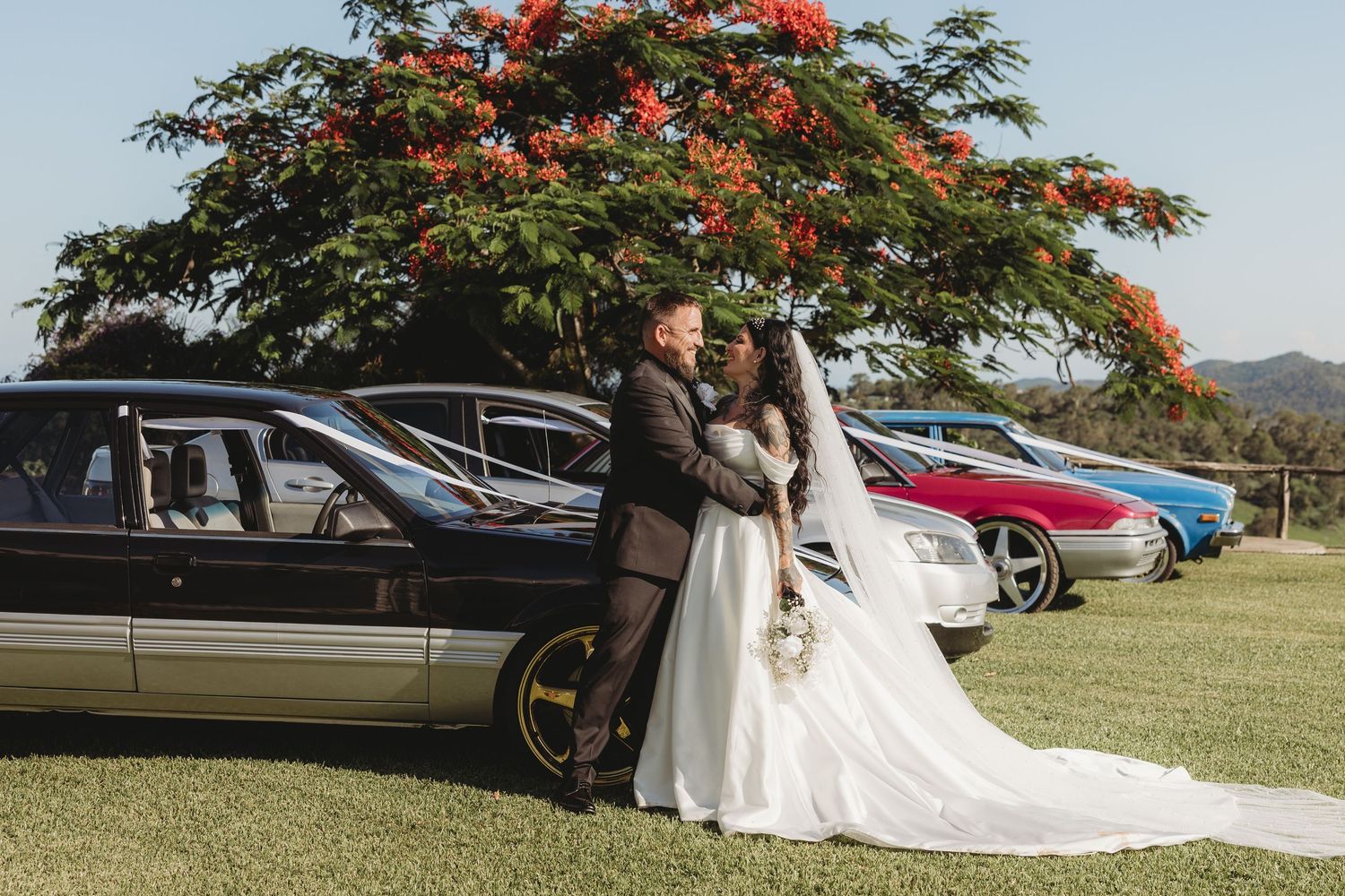 A wedding celebration scene with a beautiful floral tree and parked cars in the background.