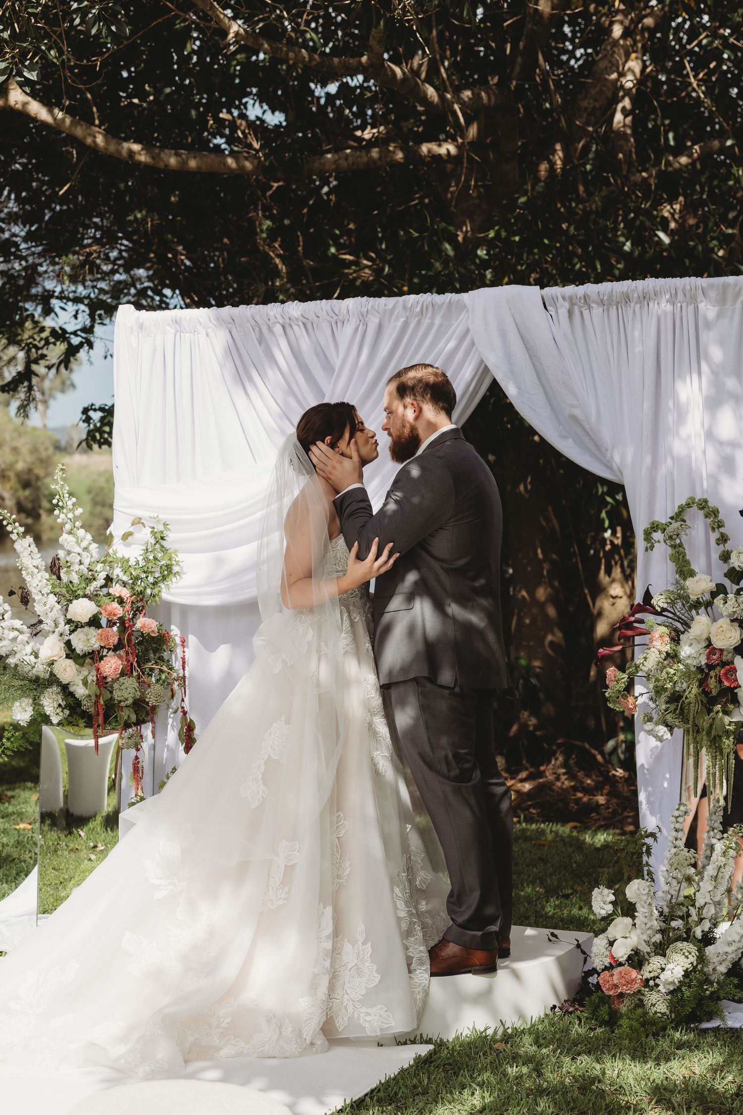 Wedding ceremony moments captured under a white fabric backdrop with floral decorations.