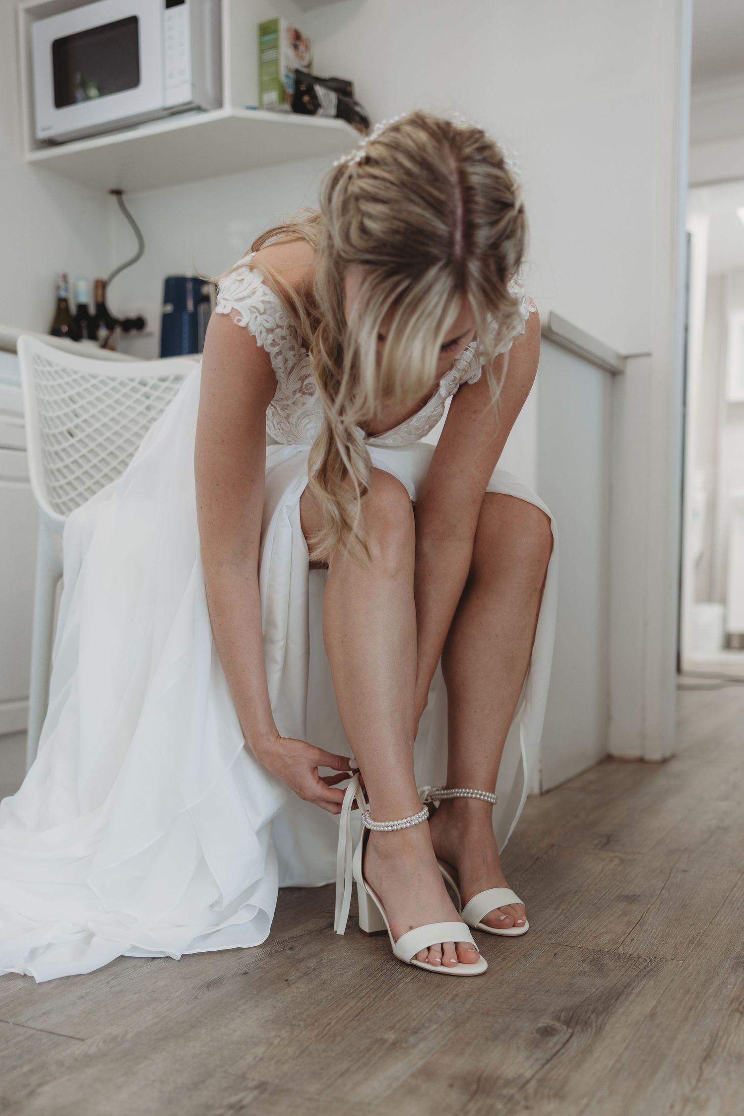 White bridal shoes being put on with wedding dress flowing on wooden floor.