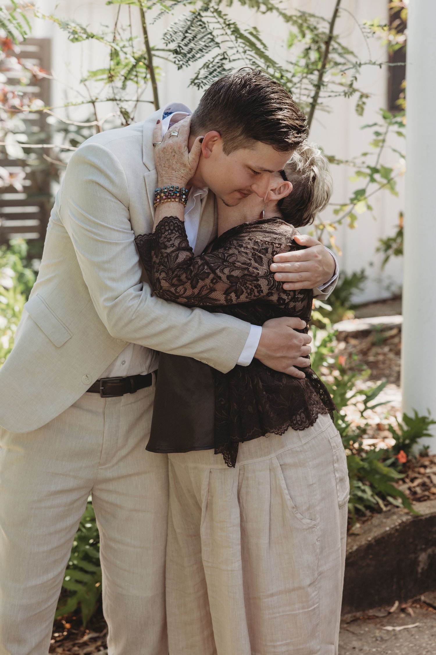 Emotional wedding moment captured in a garden setting with light colored attire.