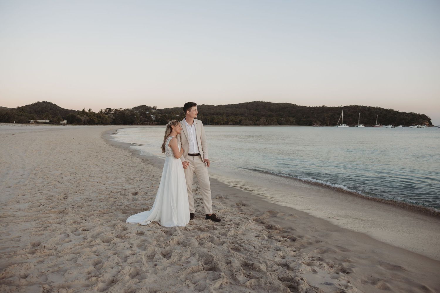 A peaceful beach scene with gentle waves and distant mountains during sunset.