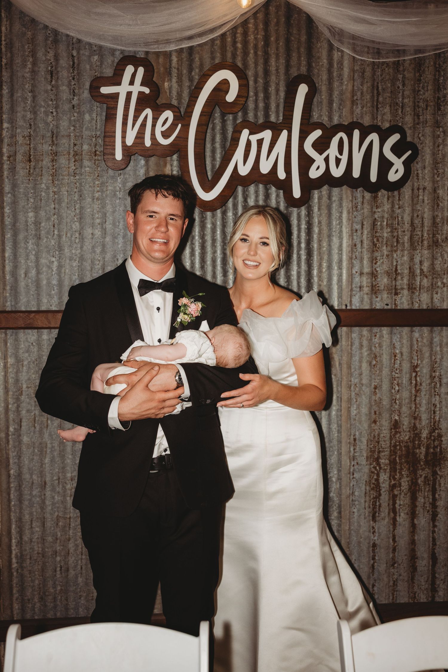 Newlyweds share a joyful moment in front of a rustic corrugated metal wall with elegant draping.