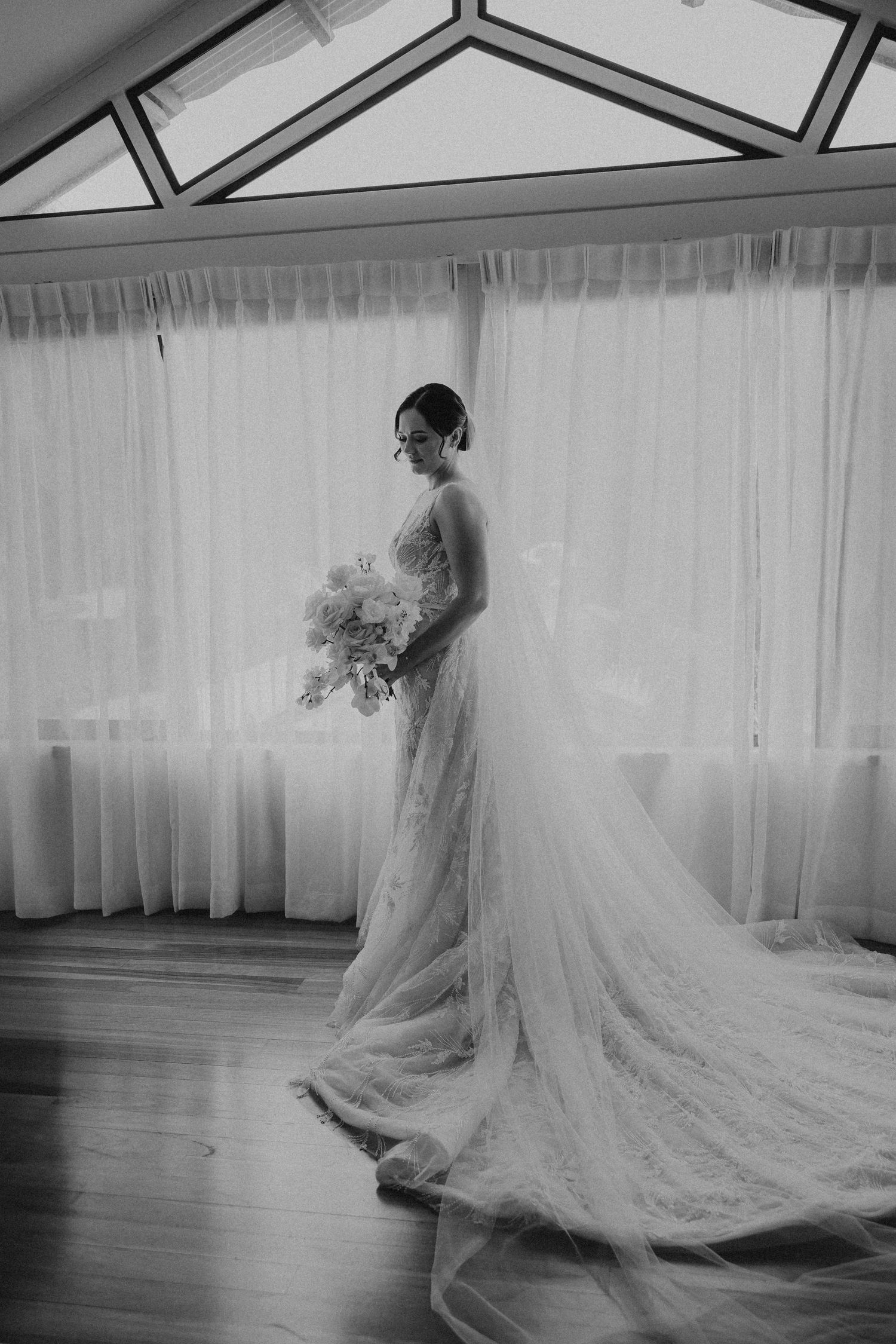 Black and white wedding photo series showing a bride's flowing veil and dress creating elegant silhouettes on a wooden floor.