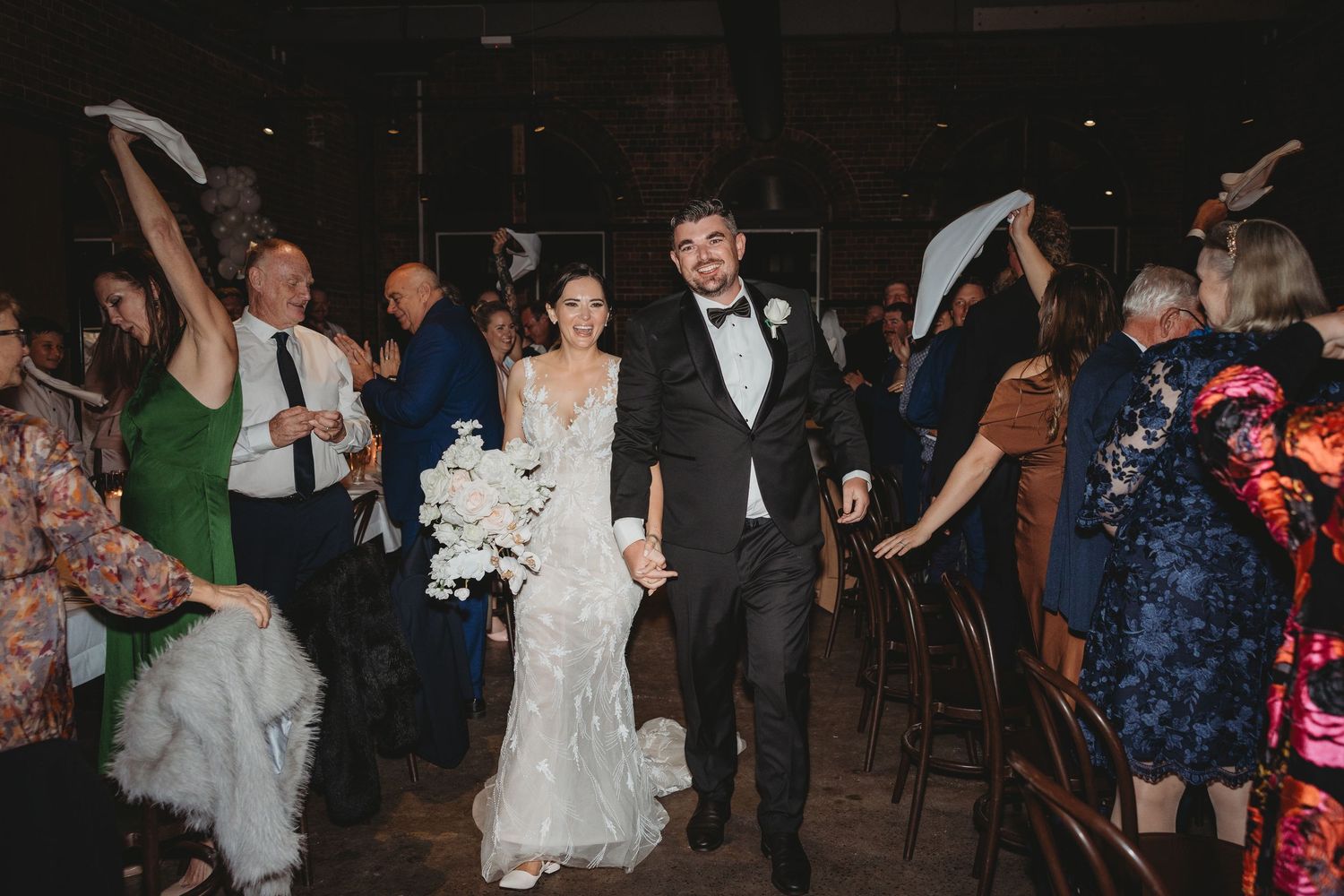 Wedding reception guests dancing and celebrating on a dark dance floor with festive lighting.