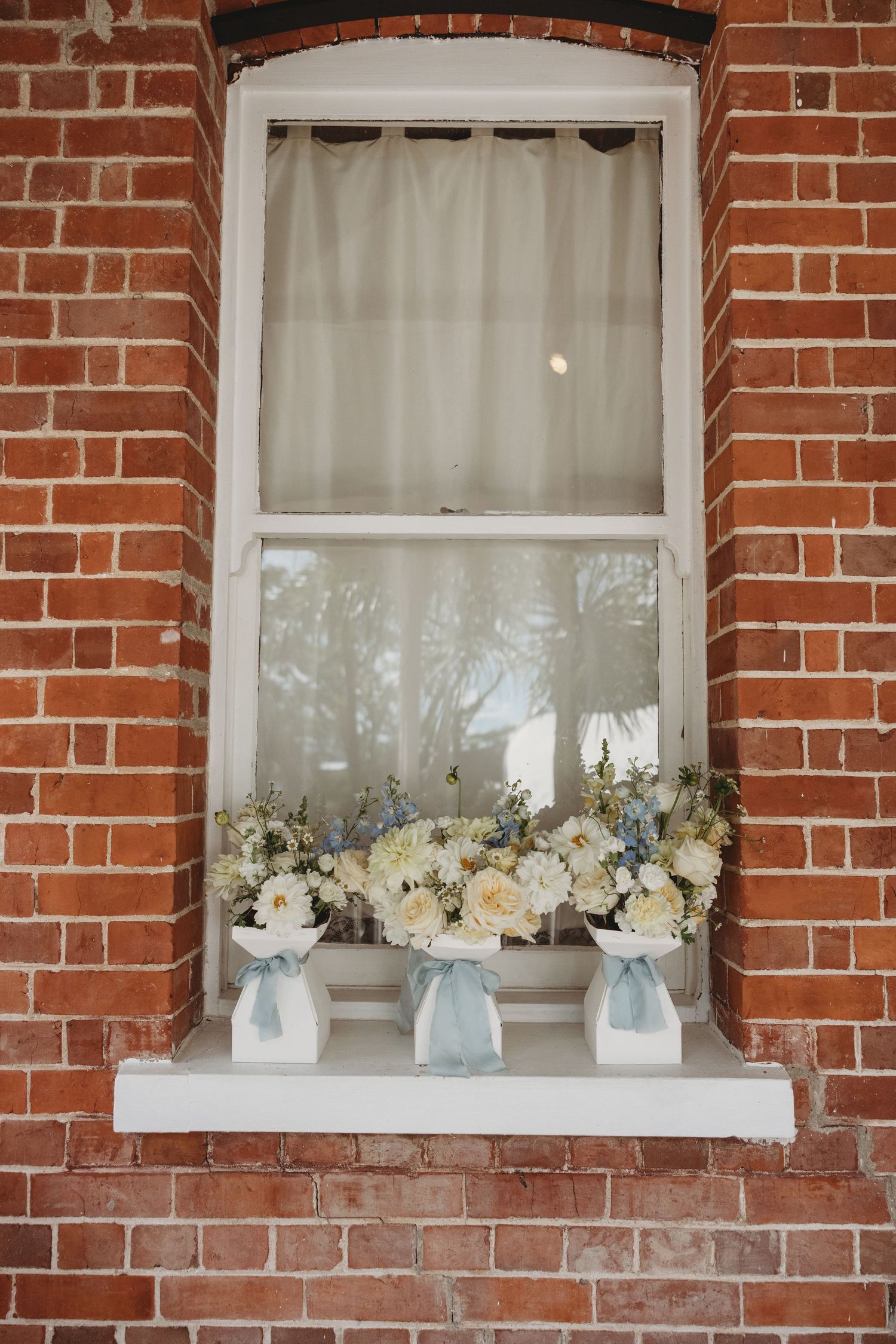 White floral arrangements displayed on windowsills of a red brick building.