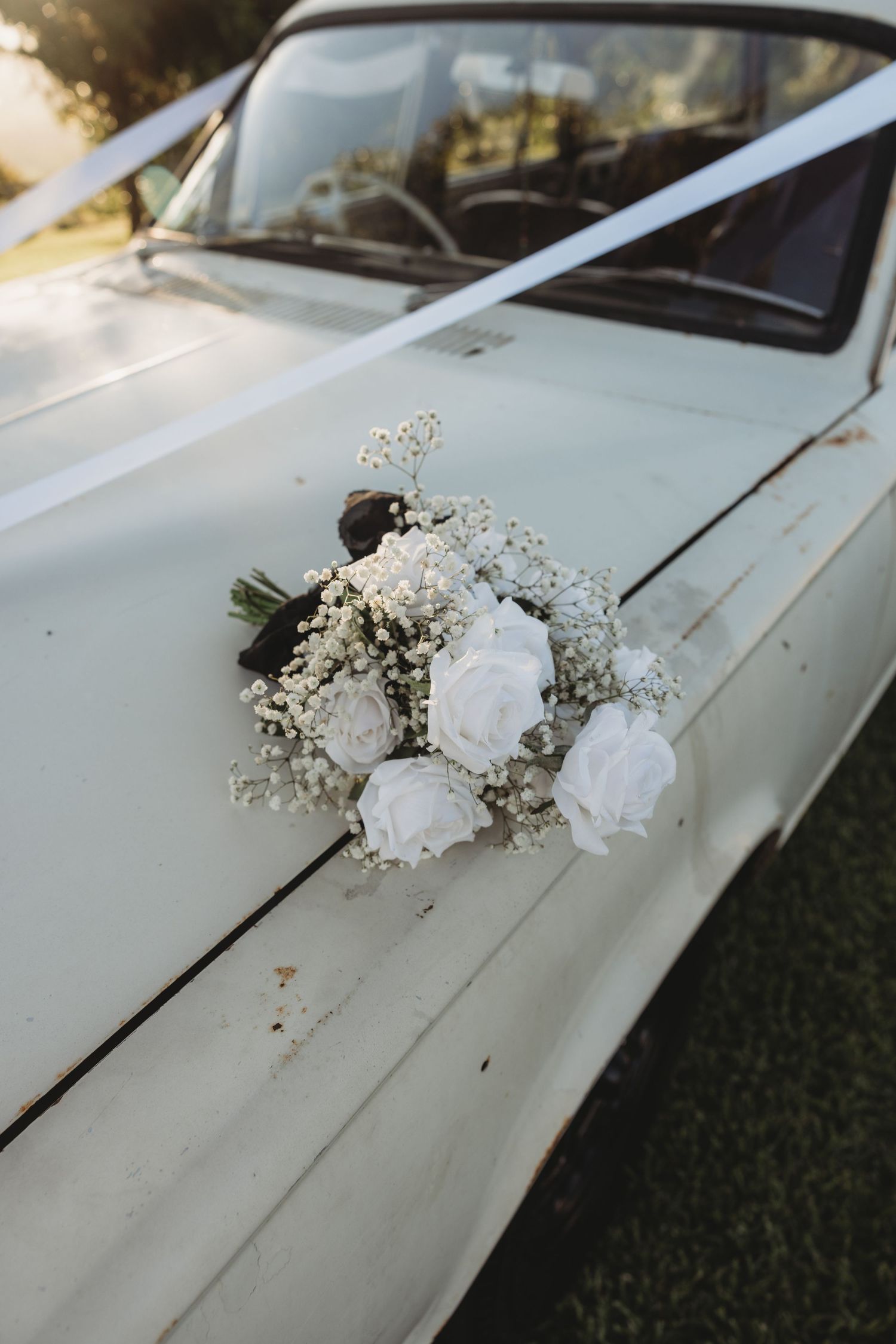 White roses and baby's breath floral decorations adorn the hood of a classic white car.