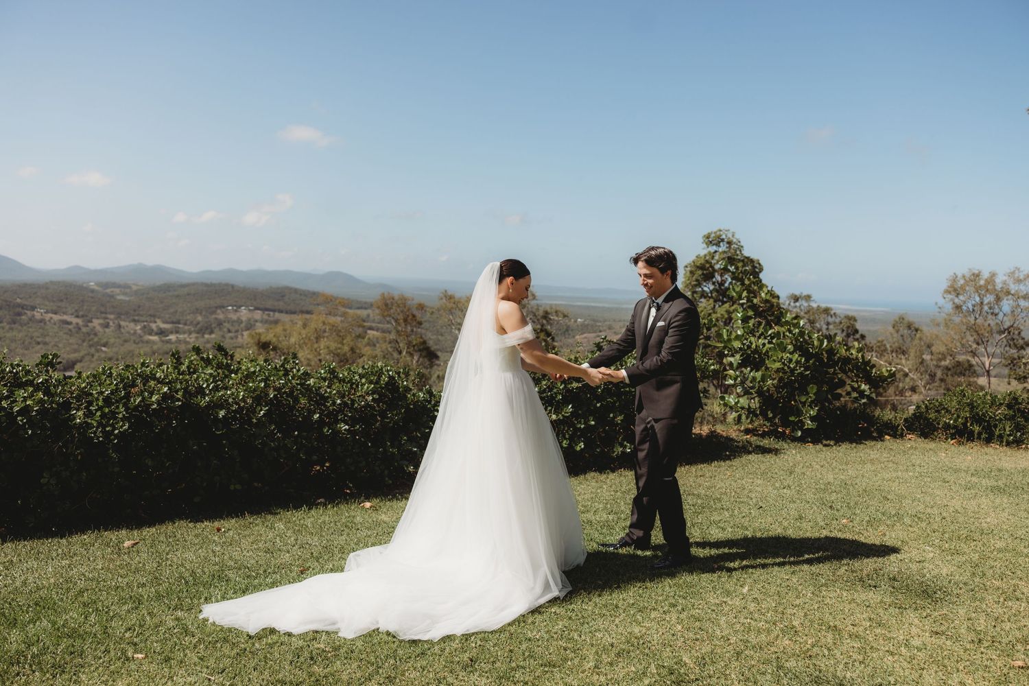 Wedding couple poses for romantic portraits on a grassy hilltop with mountain views.