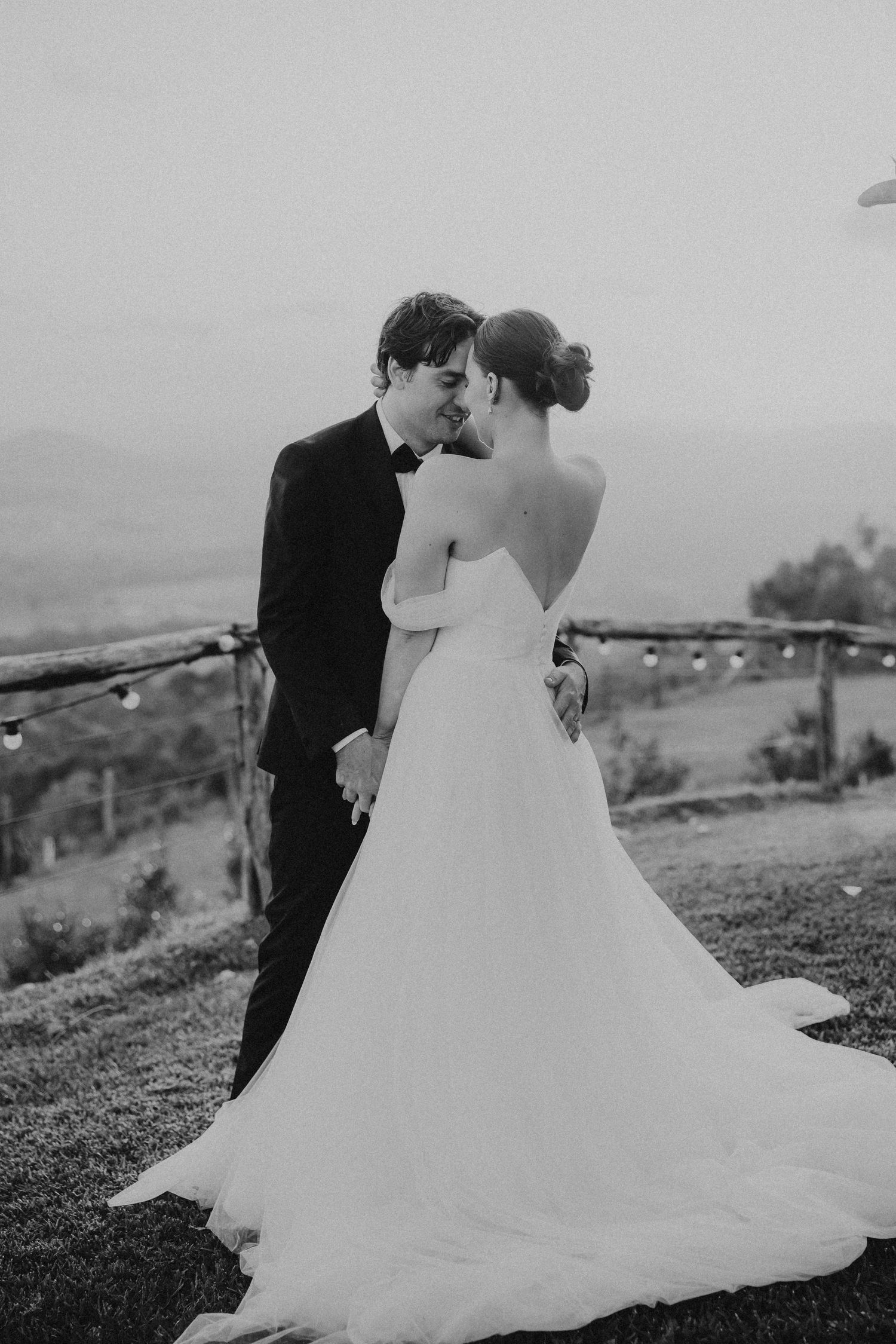 A romantic black and white wedding portrait of a couple sharing an intimate moment on a hilltop overlook.