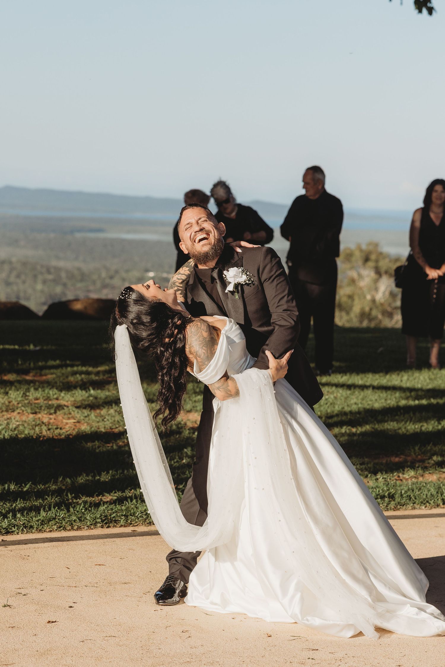 A couple shares a romantic dance dip pose outdoors with a scenic mountain view in the background.
