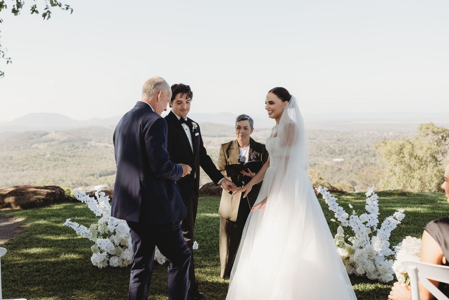 Outdoor wedding ceremony with white floral arrangements and scenic mountain backdrop.