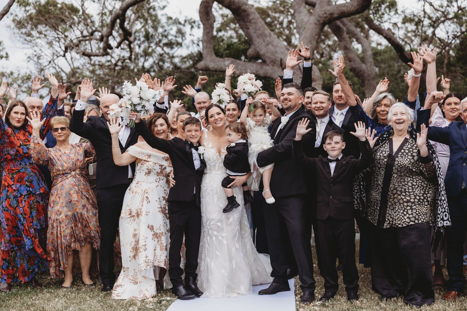 Large group of wedding guests pose for a celebratory photo outdoors.