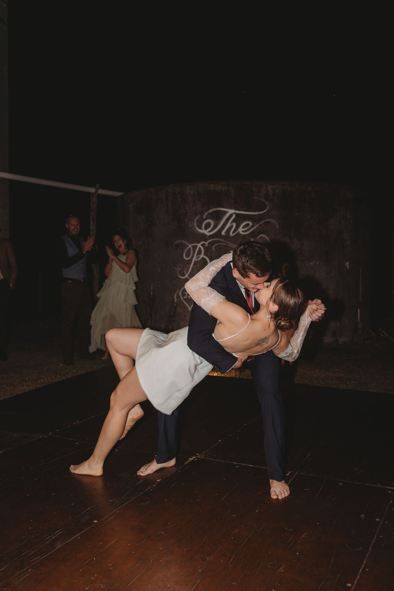 Groom dips bride in white dress during romantic first dance at outdoor wedding reception.