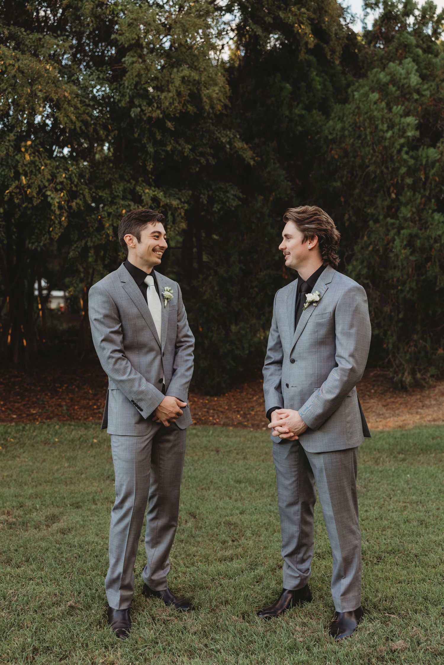 Groomsmen in matching grey suits interact casually during outdoor photo session.