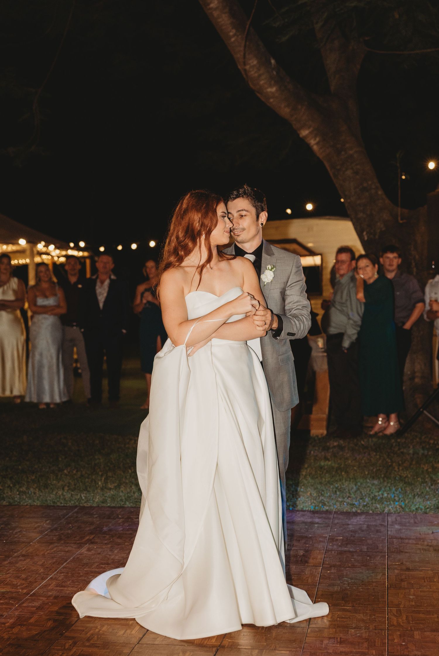 Newlyweds dancing together on an outdoor brick patio under twinkling lights.