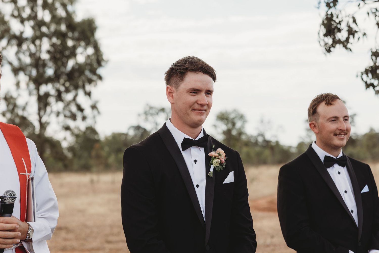 Wedding party members in formal attire standing together during an outdoor ceremony.