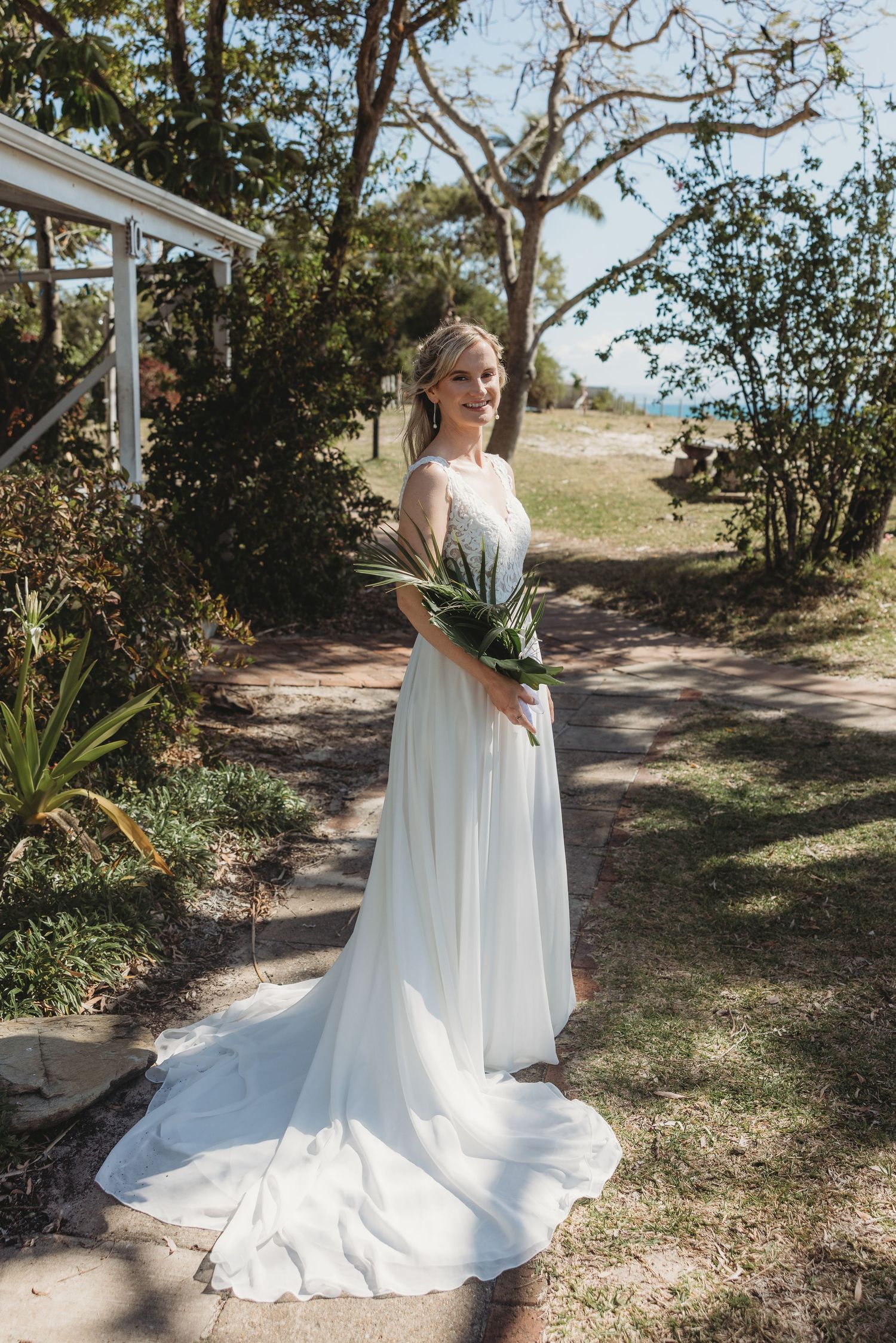 Full-length wedding dress portrait in a garden setting with natural landscaping.